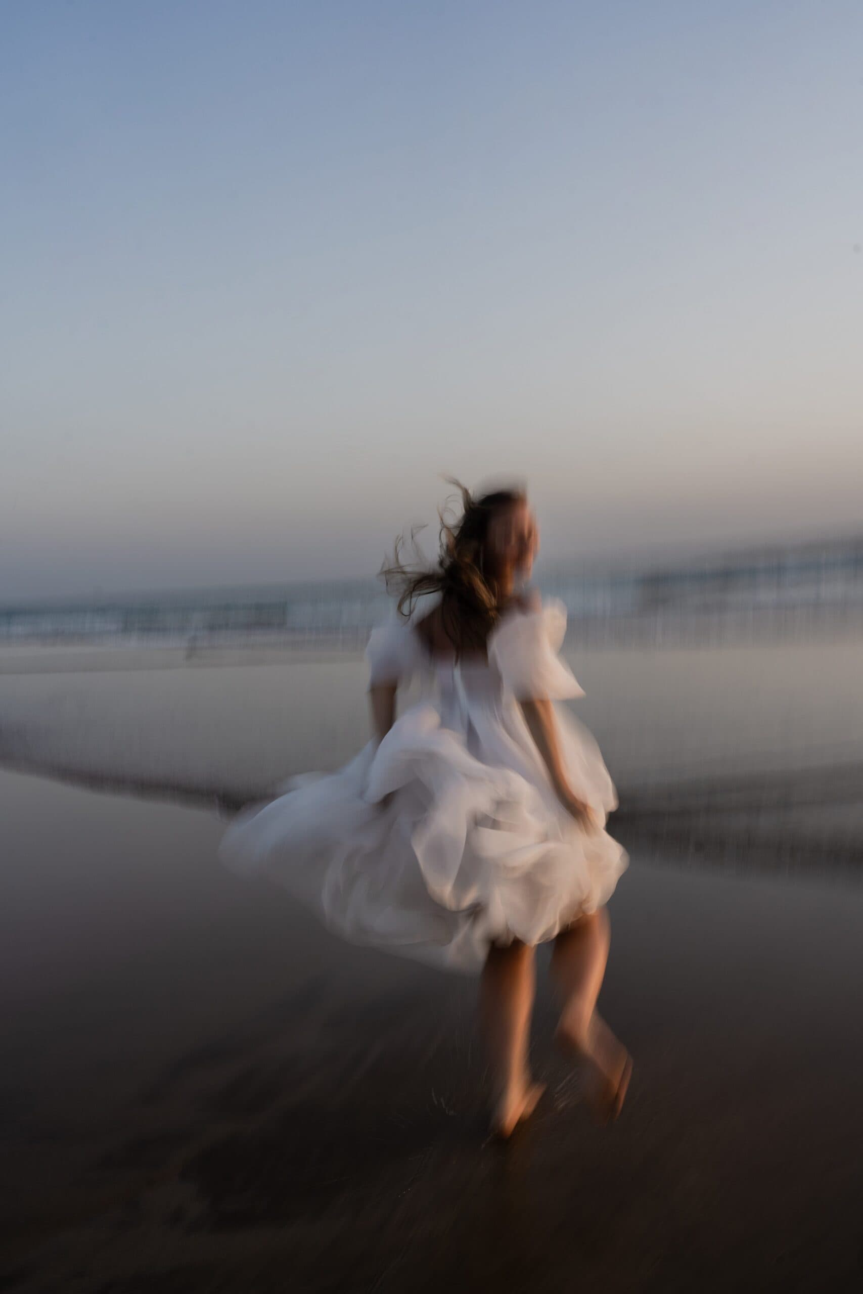 Bride running barefoot along the wet sand at Costa da Caparica in the last blue light of the evening Bride running barefoot along the wet sand at Costa da Caparica in the last blue light of the evening