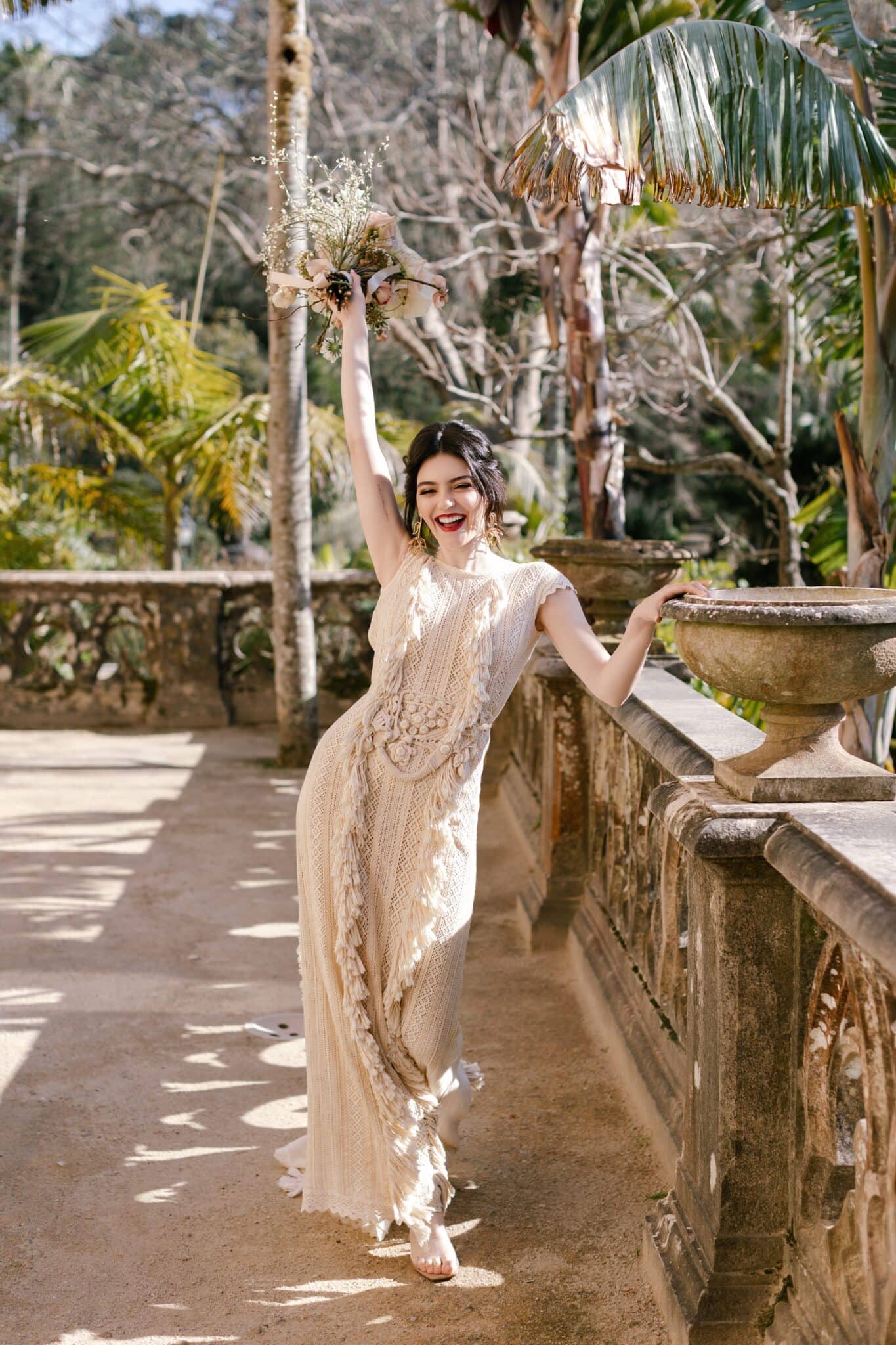 Bride raising her bouquet on the terrace of Monserrate Palace, with palms and dappled sunlight, Sintra Bride raising her bouquet on the terrace of Monserrate Palace, with palms and dappled sunlight, Sintra