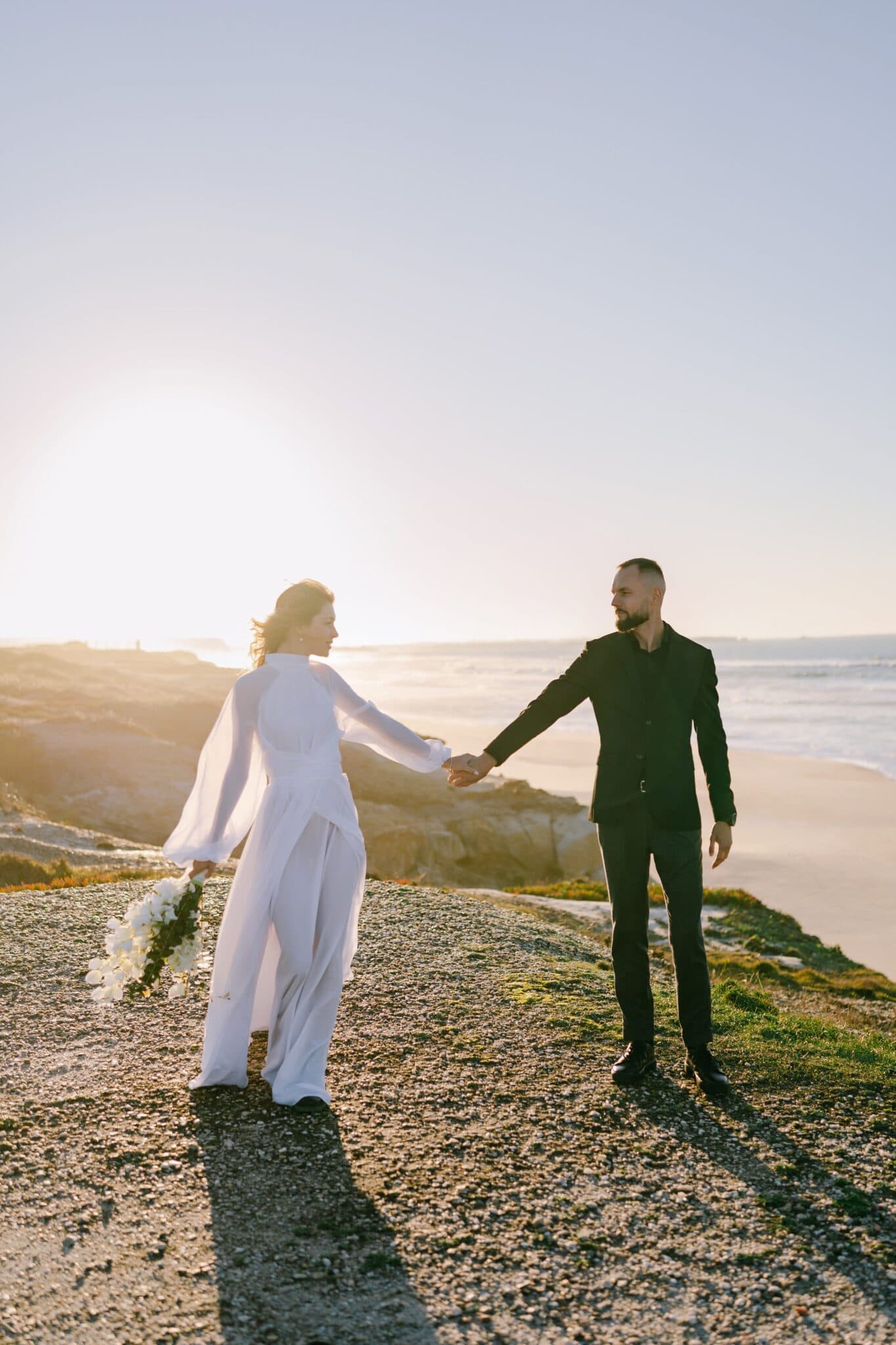 Couple holding hands on the clifftop above Praia del Rey, the low sun over the sea and the beach below Couple holding hands on the clifftop above Praia del Rey, the low sun over the sea and the beach below