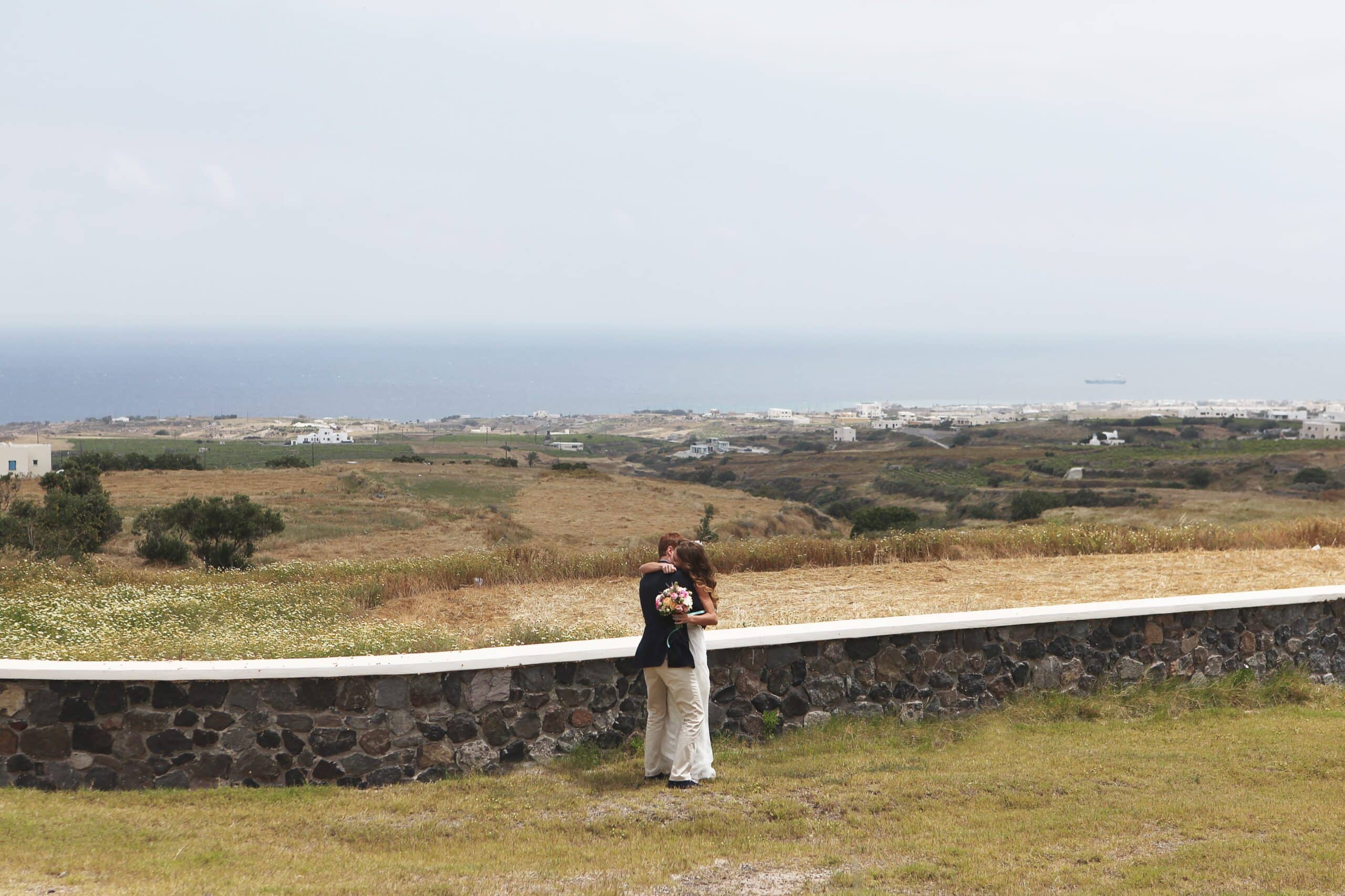Bride and groom embracing in a vast field overlooking the sea on their wedding day Bride and groom embracing in a vast field overlooking the sea on their wedding day
