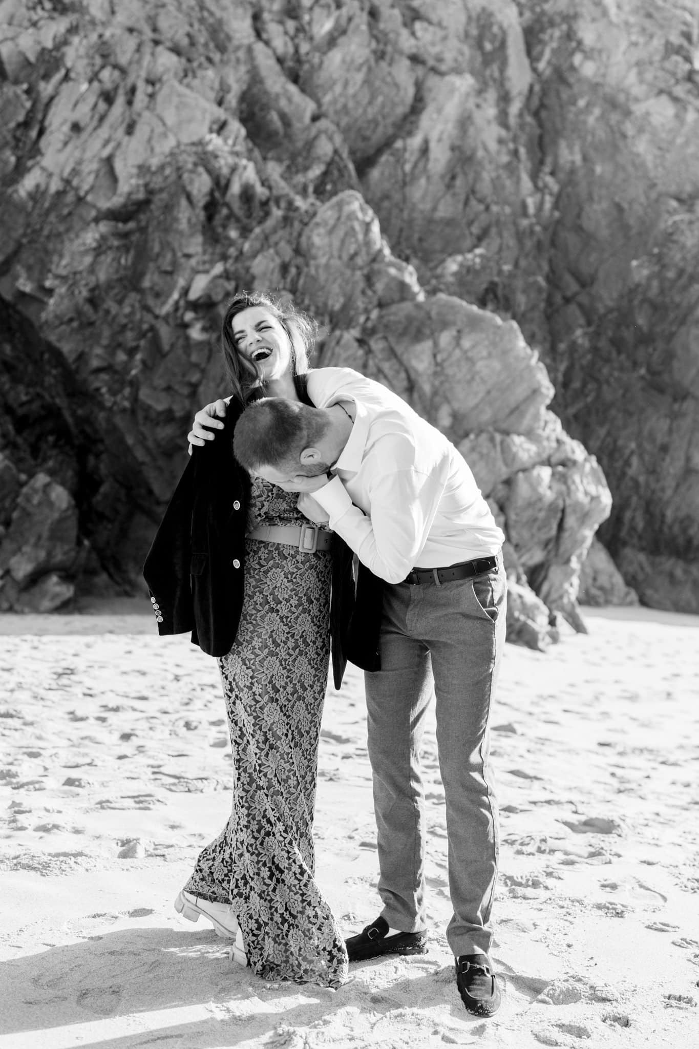 Couple laughing and hugging on the sand at Praia da Ursa right after the proposal, black and white Couple laughing and hugging on the sand at Praia da Ursa right after the proposal, black and white