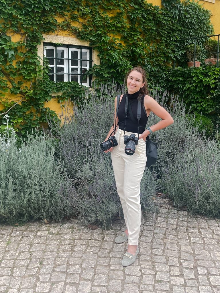Yana Yart, wedding photographer, with her camera by an ivy-covered house