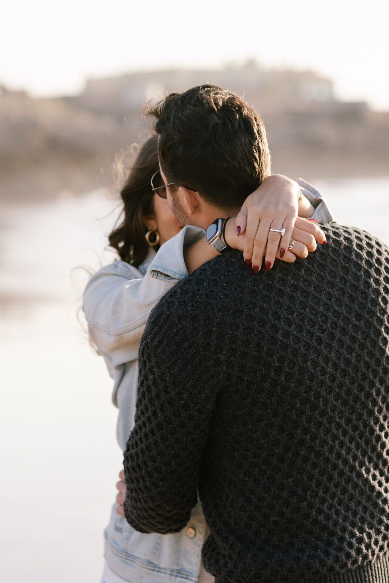 Woman's hand with an engagement ring on her partner's knit sweater as they hug at Guincho, Cascais Woman's hand with an engagement ring on her partner's knit sweater as they hug at Guincho, Cascais