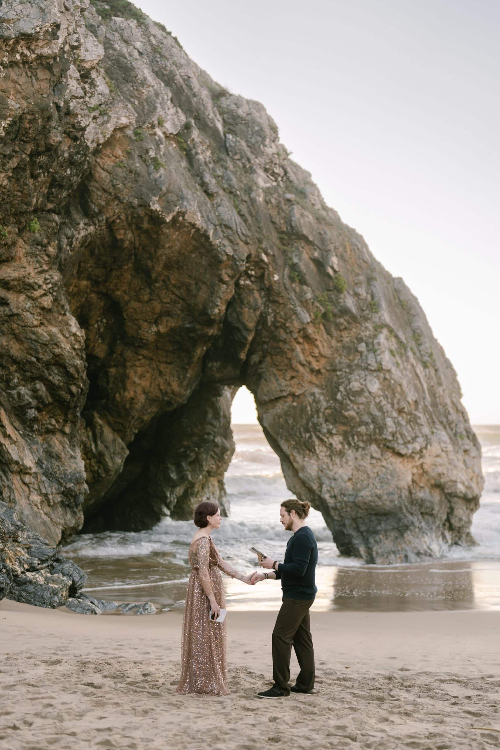 Couple exchanging vows beneath the natural rock arch at Praia da Adraga, Sintra Couple exchanging vows beneath the natural rock arch at Praia da Adraga, Sintra