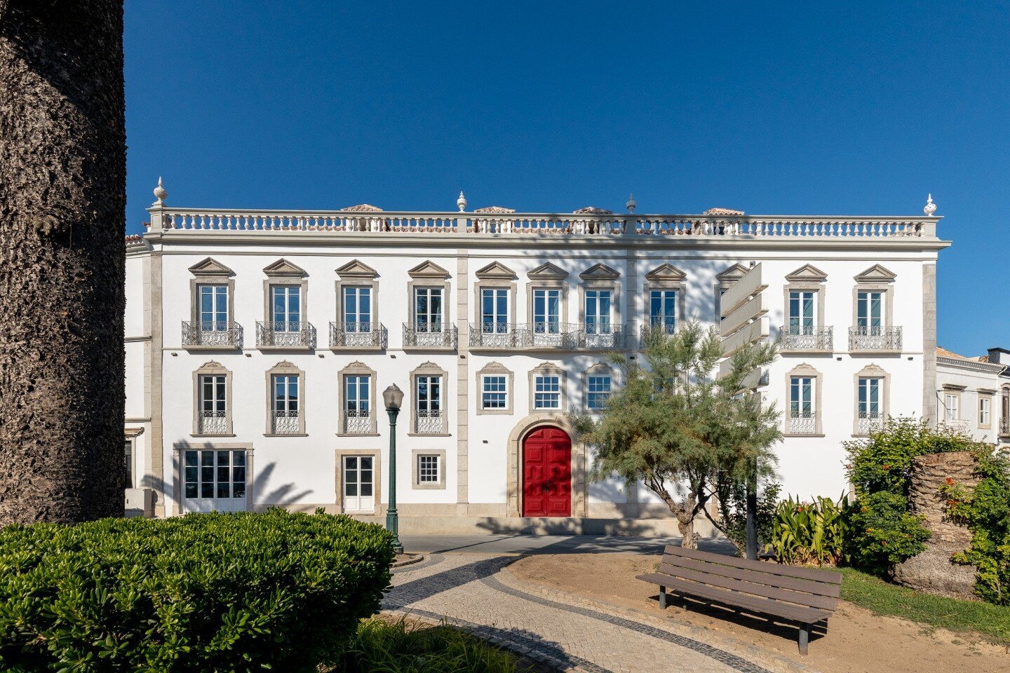 The white facade of the Palácio de Tavira with its red door and garden The white facade of the Palácio de Tavira with its red door and garden