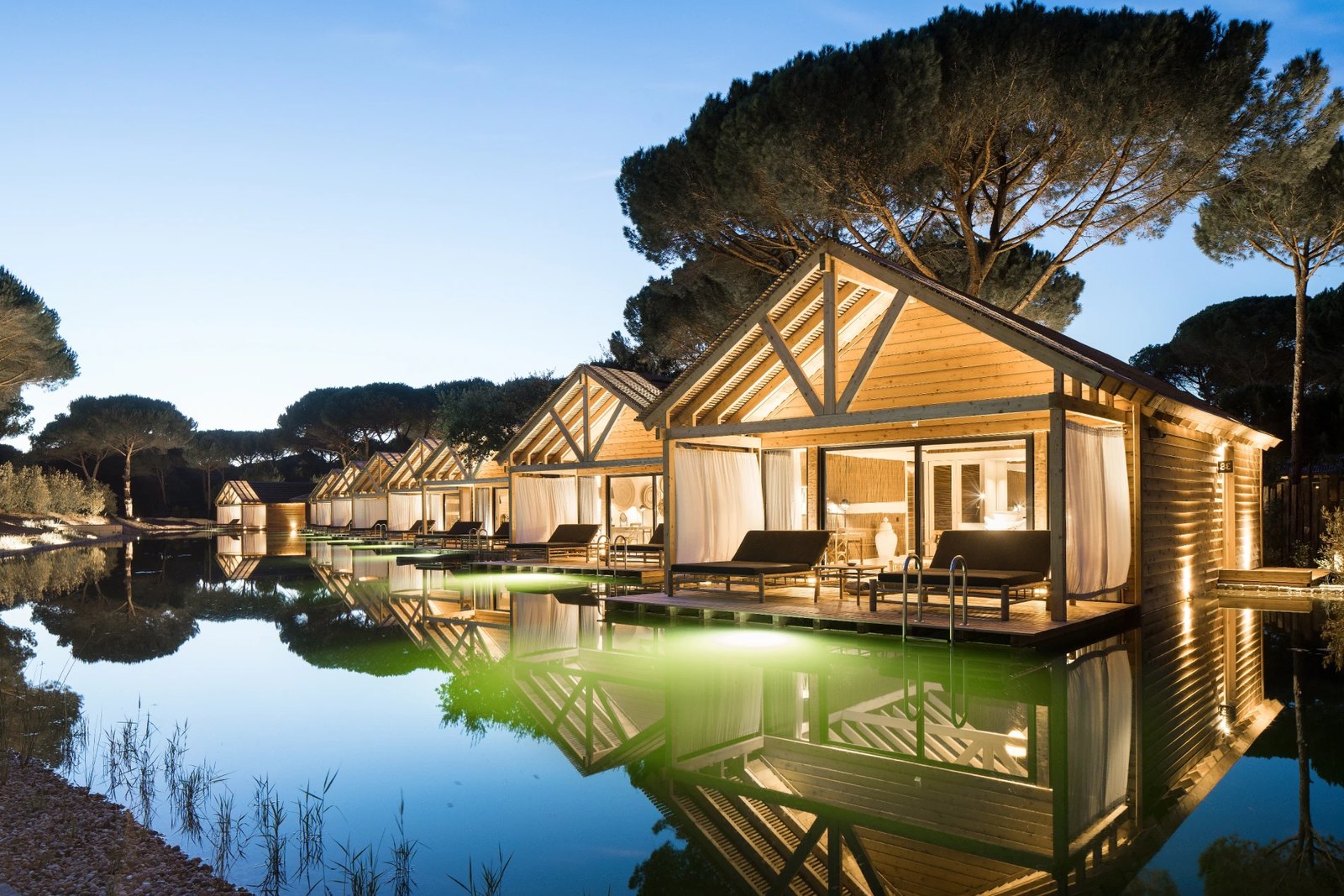 Timber cabanas among the pines reflected in a pond at dusk, Sublime Comporta Timber cabanas among the pines reflected in a pond at dusk, Sublime Comporta