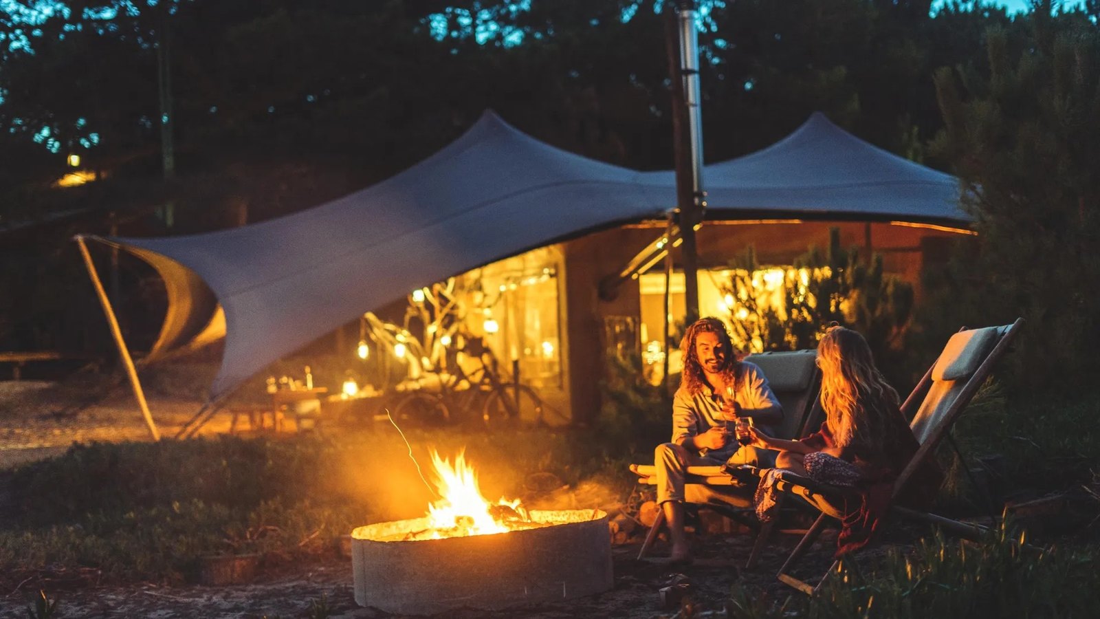 Guests around a fire pit in front of a lit tent under the trees at night, Areias do Seixo, Santa Cruz Guests around a fire pit in front of a lit tent under the trees at night, Areias do Seixo, Santa Cruz