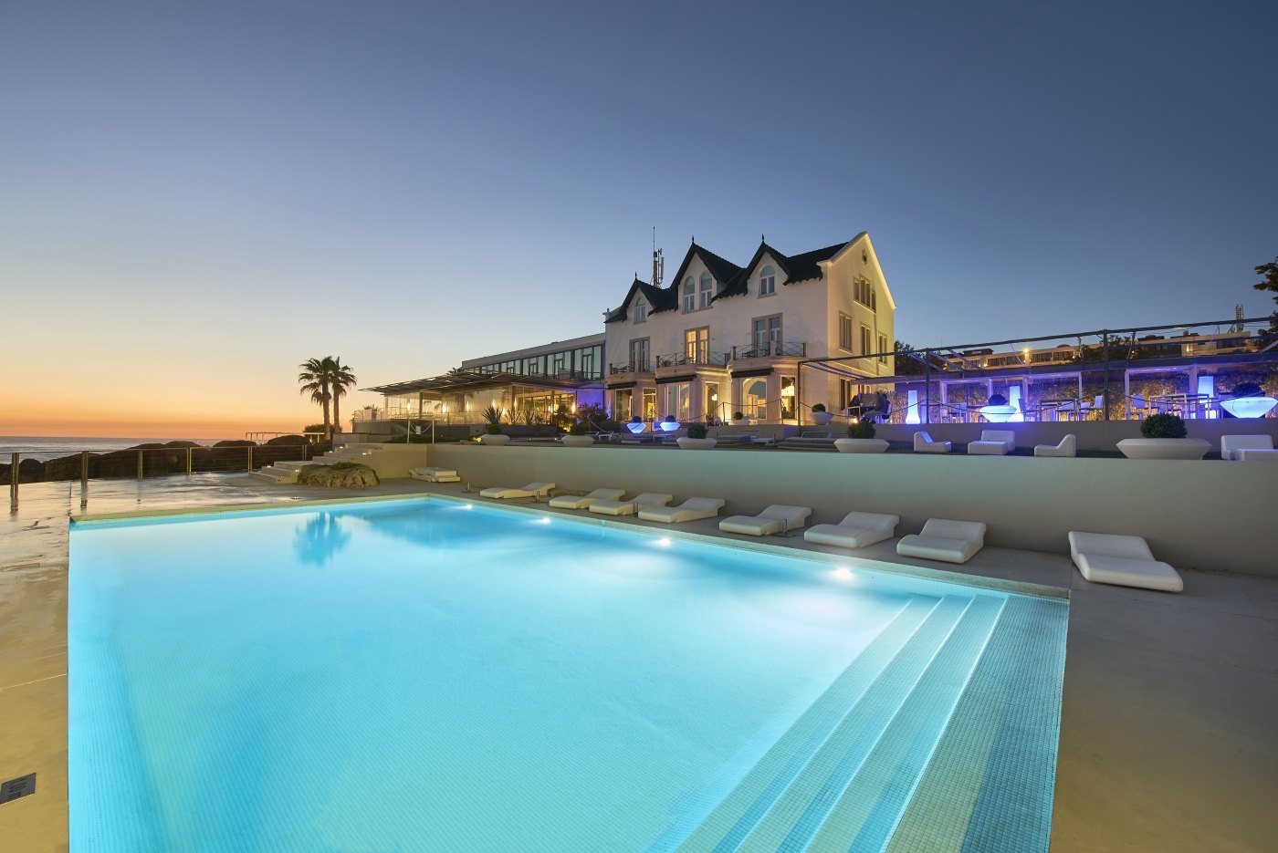The pool and the white mansion of the Farol Hotel at dusk above the ocean, Cascais The pool and the white mansion of the Farol Hotel at dusk above the ocean, Cascais
