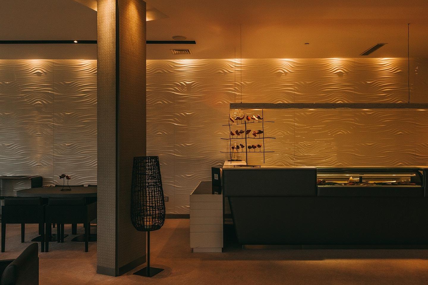Dining room with wave-patterned wall panels in warm evening light at Midori, Penha Longa, Sintra