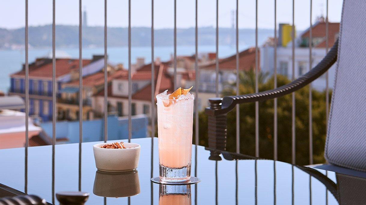 A cocktail on the terrace railing with Lisbon's rooftops and the river behind, BAHR terrace, Bairro Alto Hotel