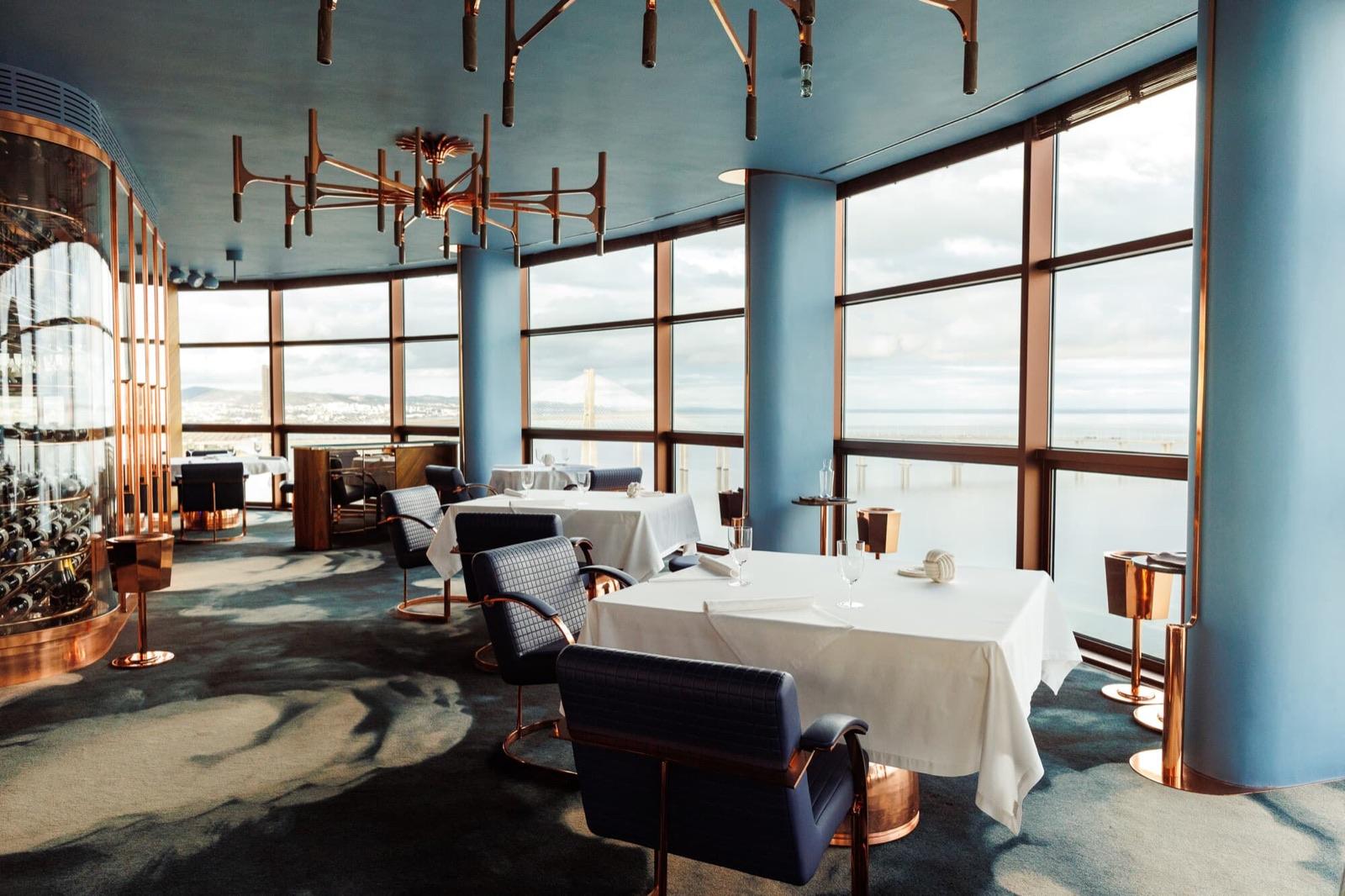 Round glass dining room with copper chandeliers and white tables looking over the Tagus at Fifty Seconds, Lisbon