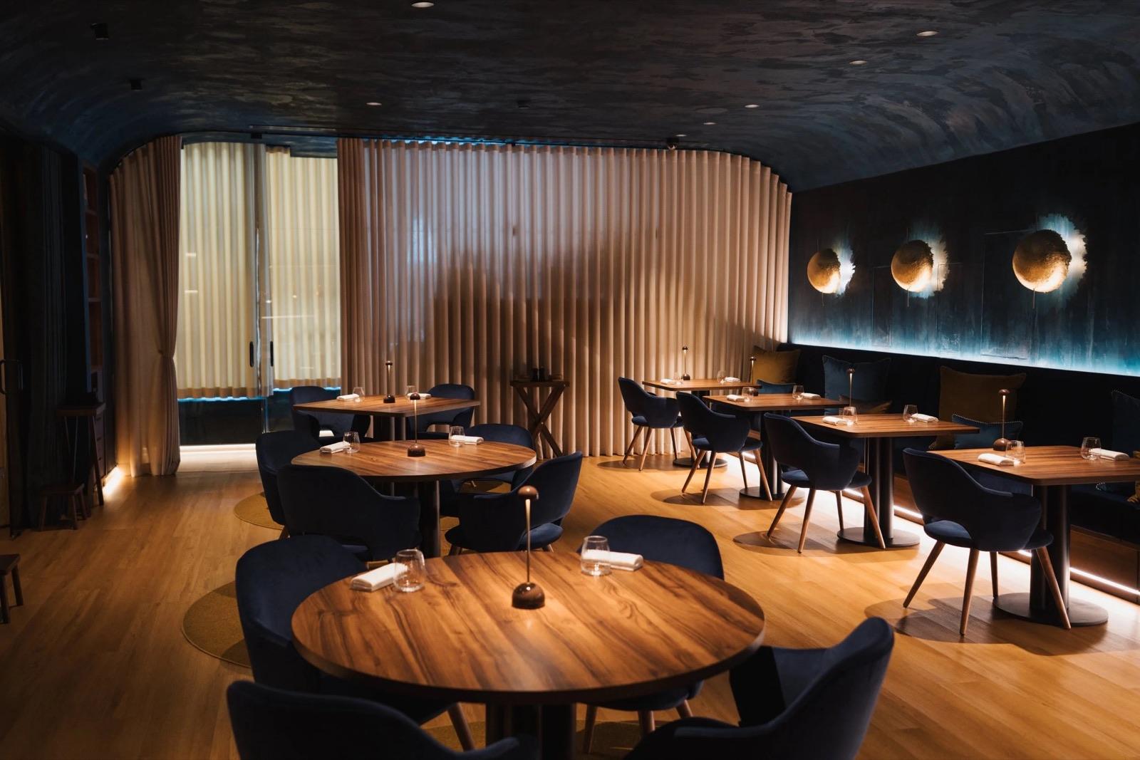 Dark, intimate dining room with round wooden tables and soft wall lights at Henrique Sá Pessoa, Lisbon