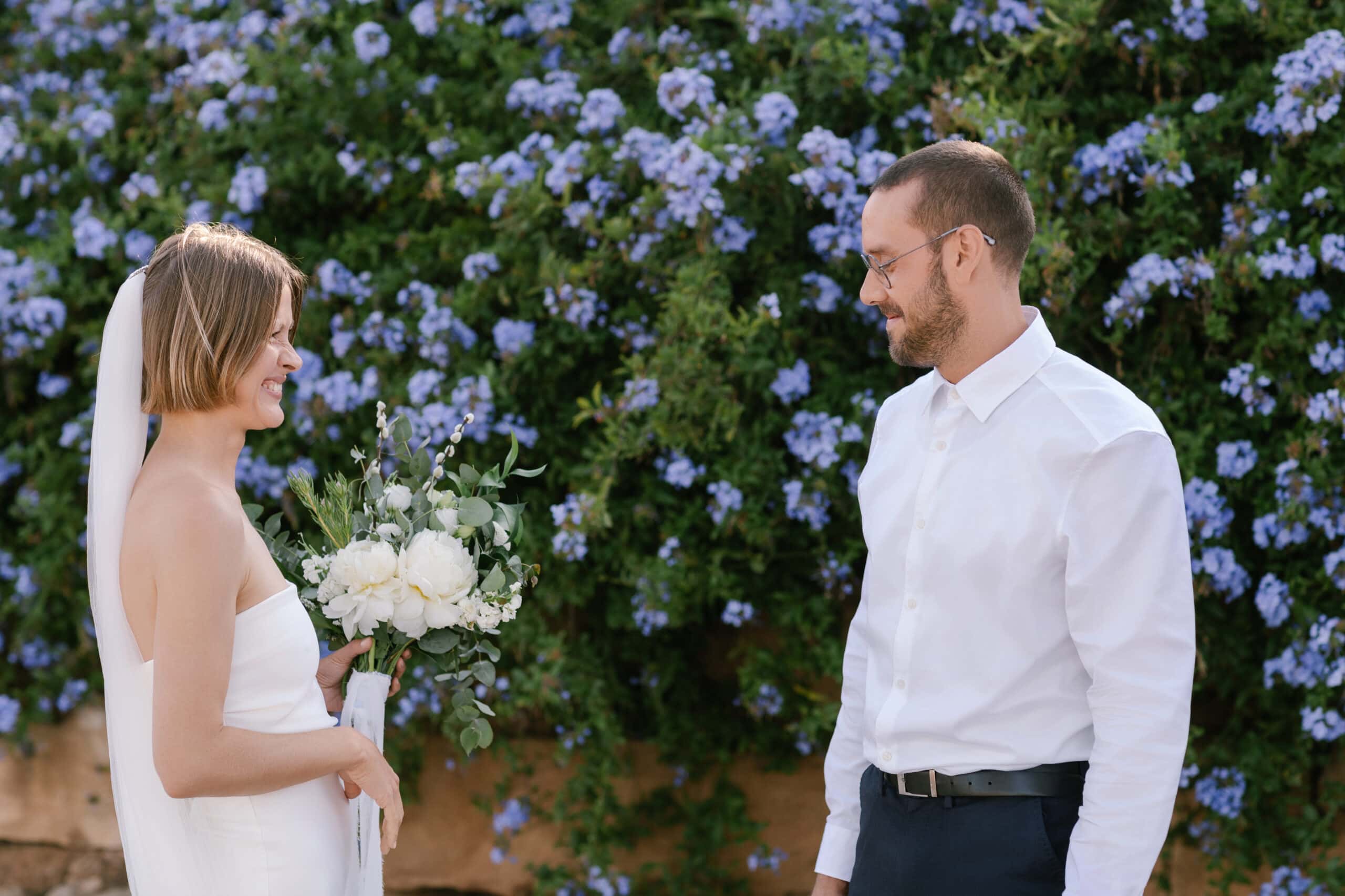 Bride and groom smiling at each other during their First Look in an Algarve garden with blue flowers