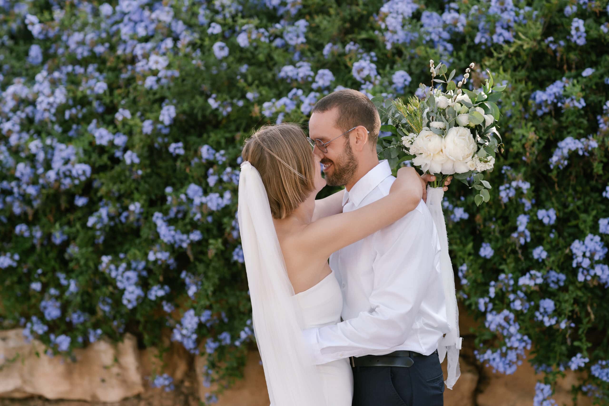 Bride and groom embracing during their First Look, surrounded by blue flowers in Algarve.