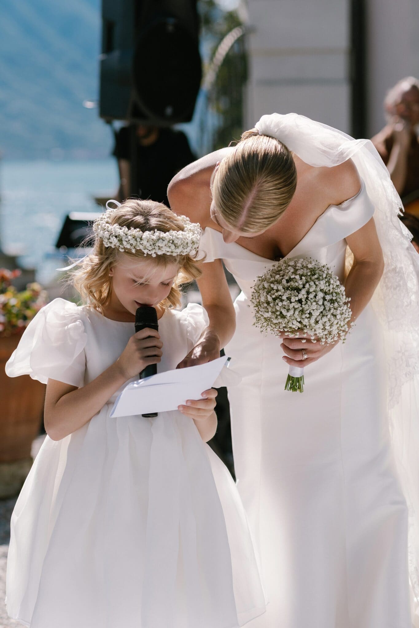 Bride leaning toward flower girl reading a note during wedding ceremony at Villa Carlotta