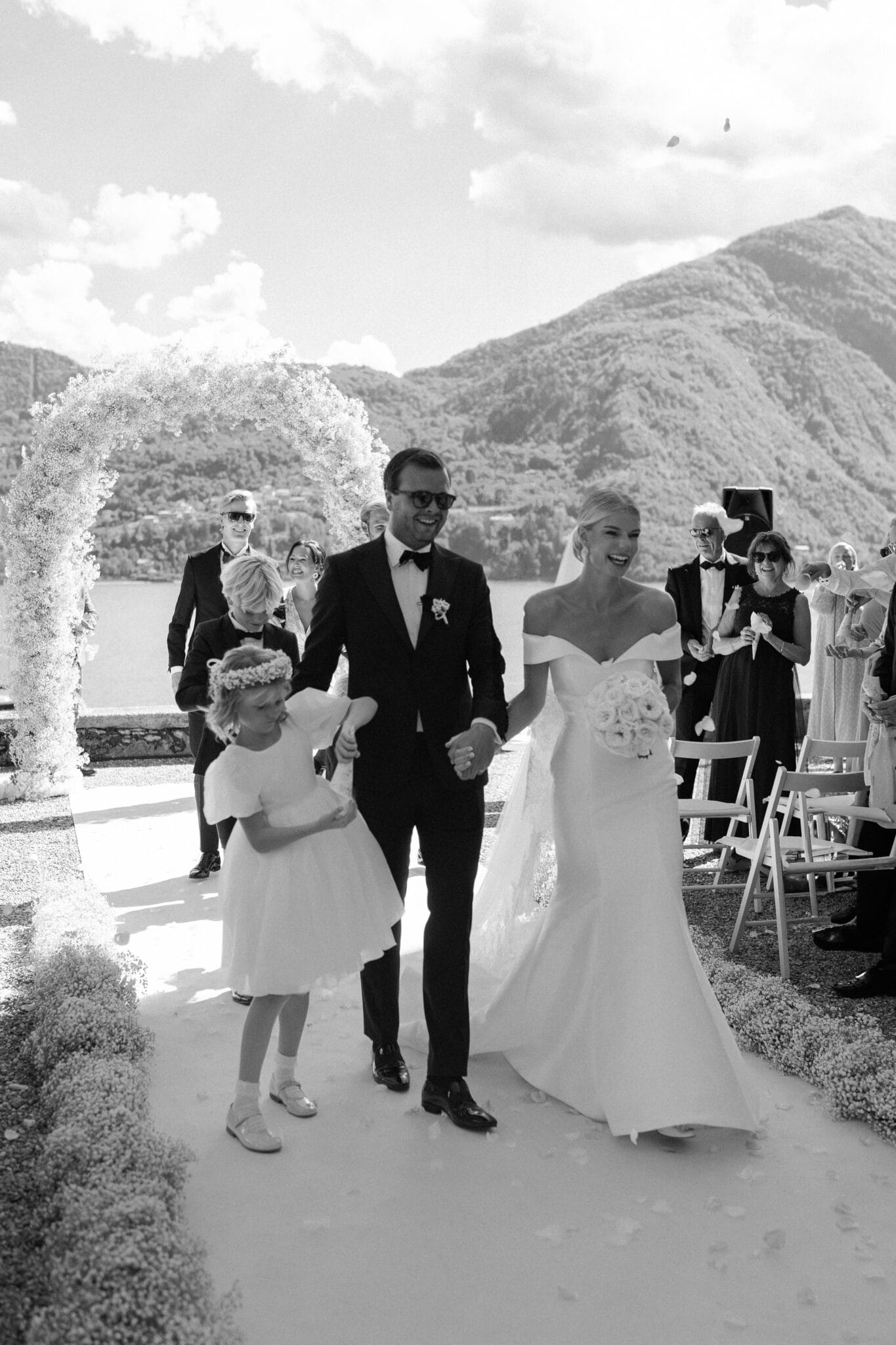 Bride and groom walking joyfully with a flower girl after their wedding ceremony at Villa Carlotta.