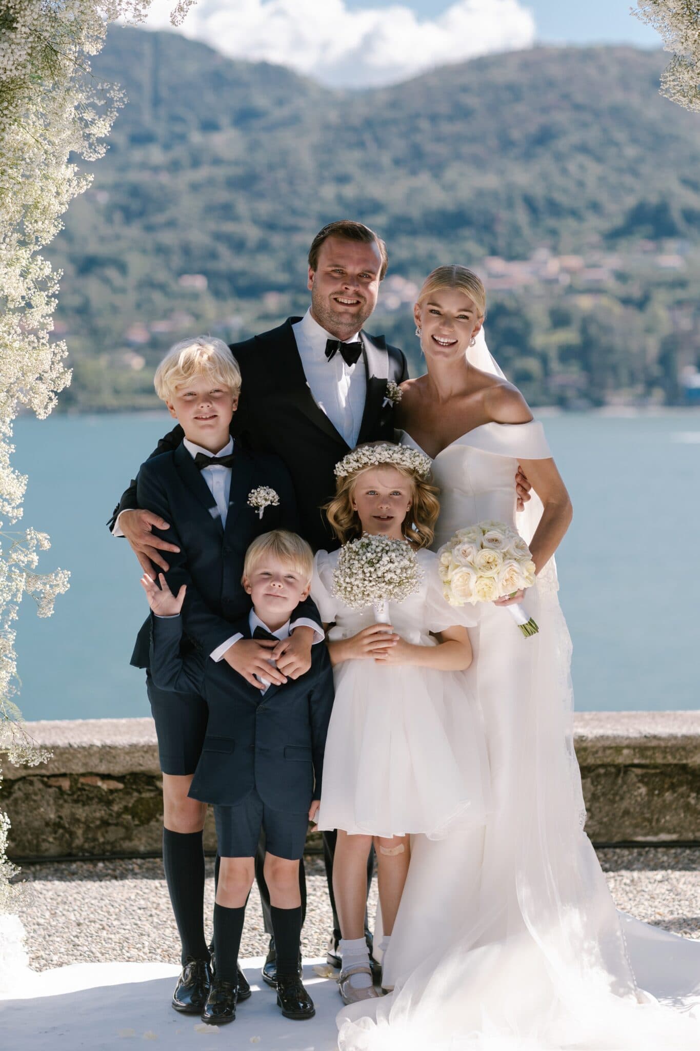 Bride and groom with children smiling together at Villa Carlotta with Lake Como backdrop.