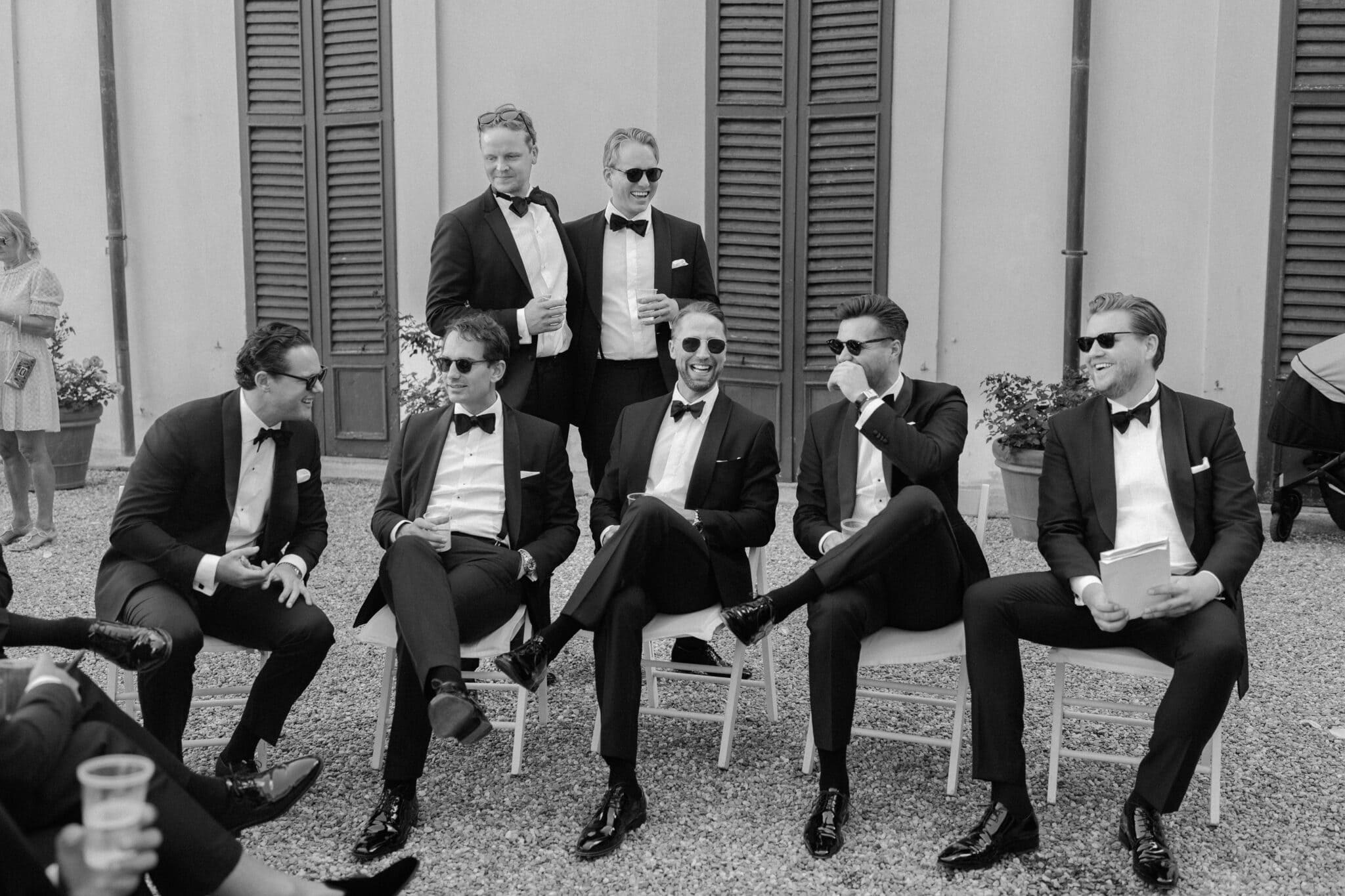 Group of groomsmen laughing together outside Villa Carlotta, captured in black and white.
