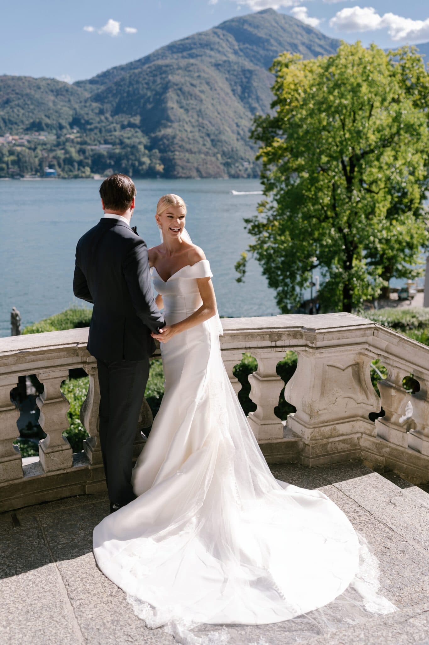 Bride and groom standing on Villa Carlotta’s terrace overlooking Lake Como, with majestic mountains in the background