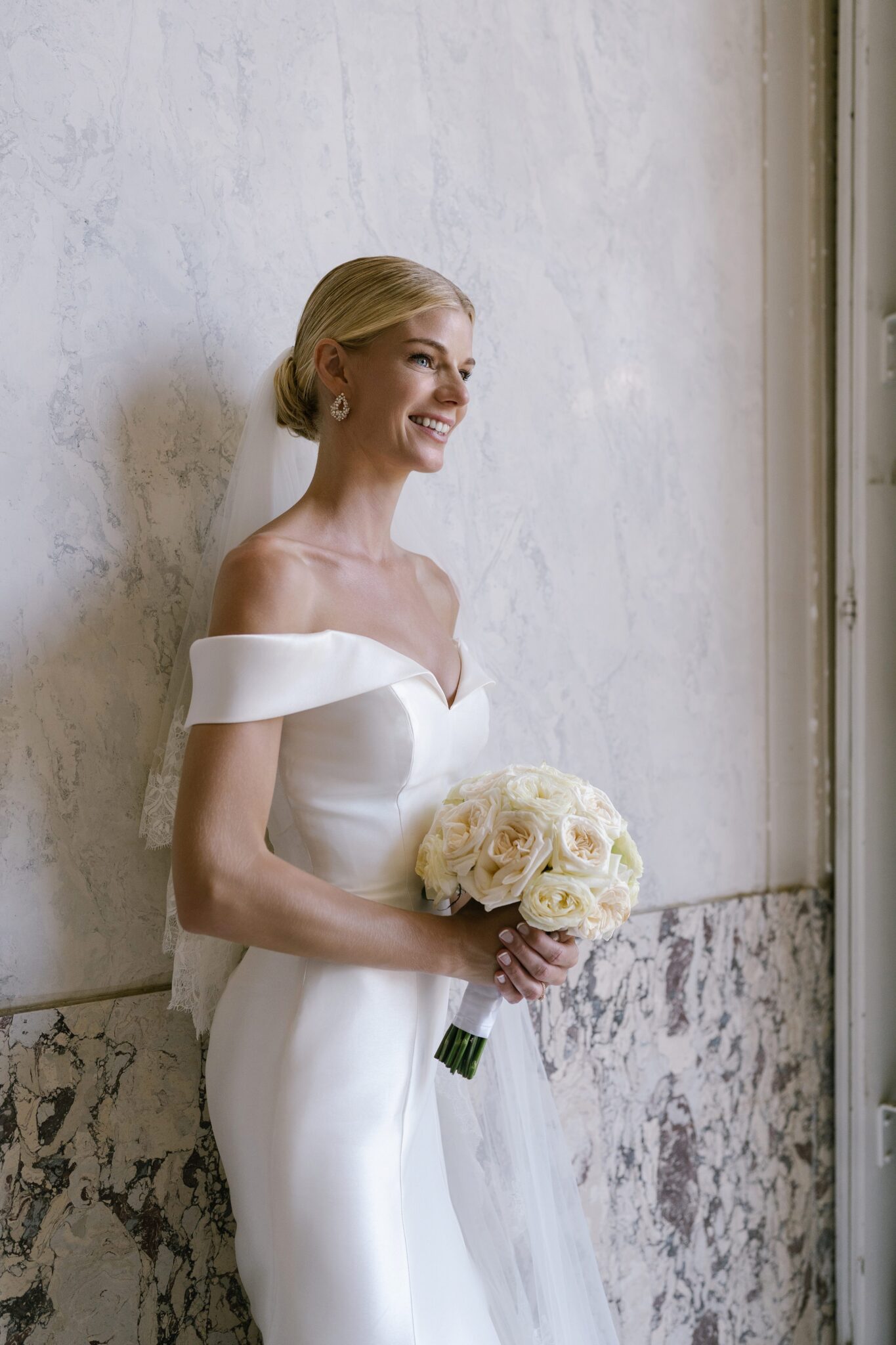 Bride holding a white rose bouquet, smiling softly against the marble walls of Villa Carlotta on her Lake Como wedding day.