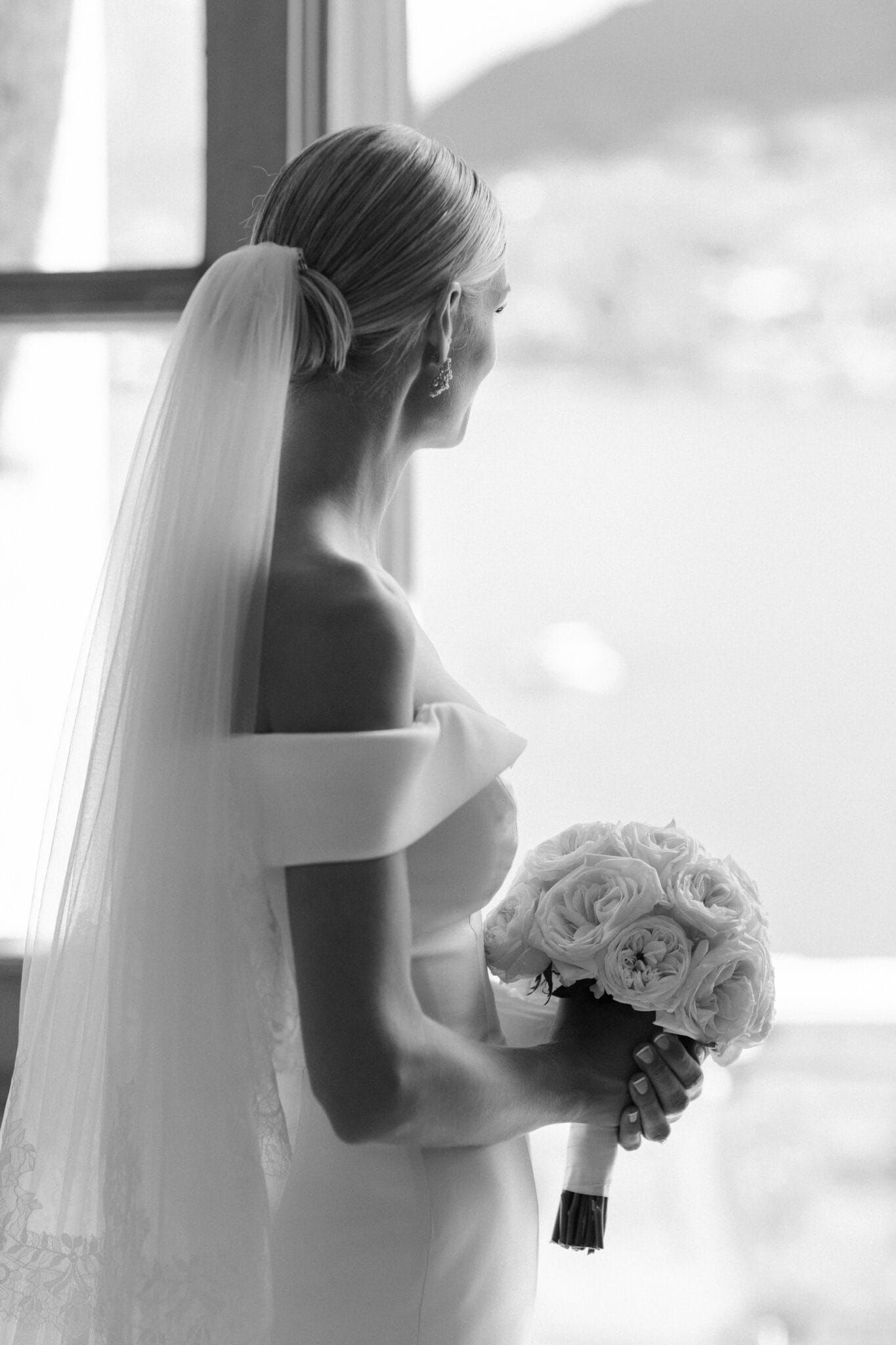 Bride holding bouquet while gazing out of the window at Villa Carlotta, captured in black and white.
