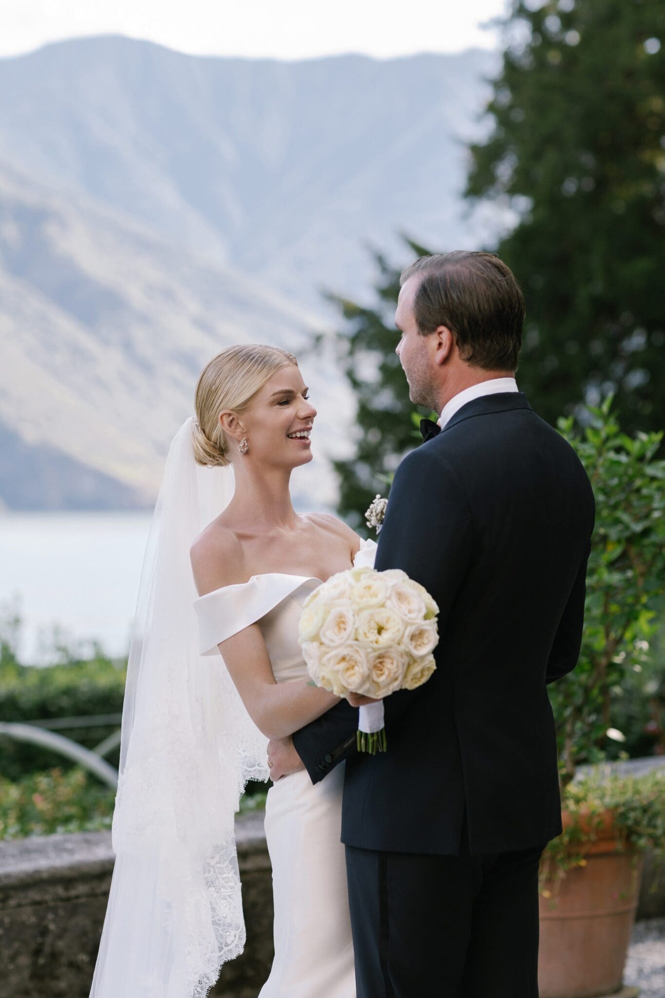 Bride and groom smiling with bouquet in hand and Lake Como behind them.