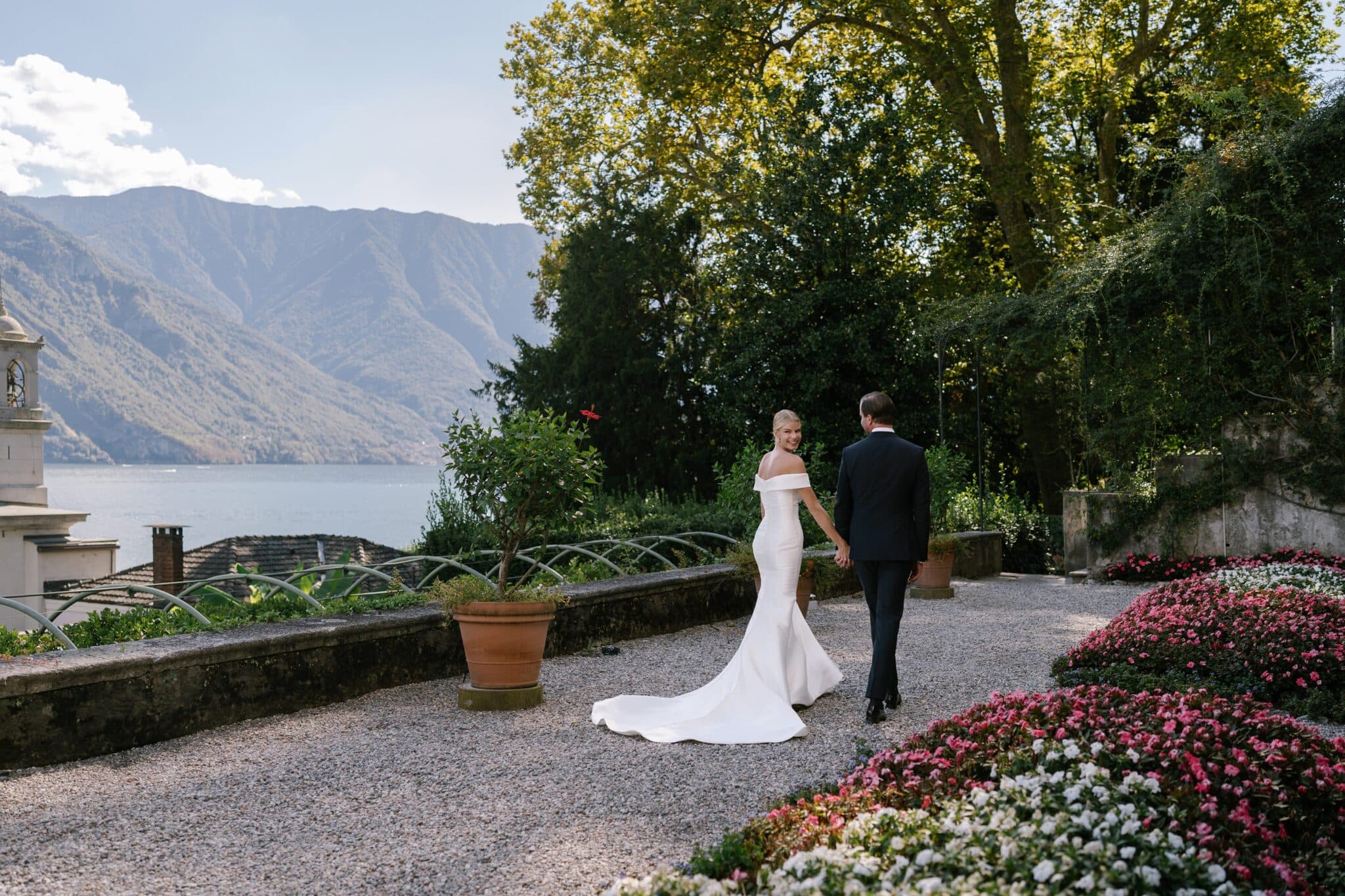 Bride smiling back at the camera while walking hand in hand with the groom by Lake Como