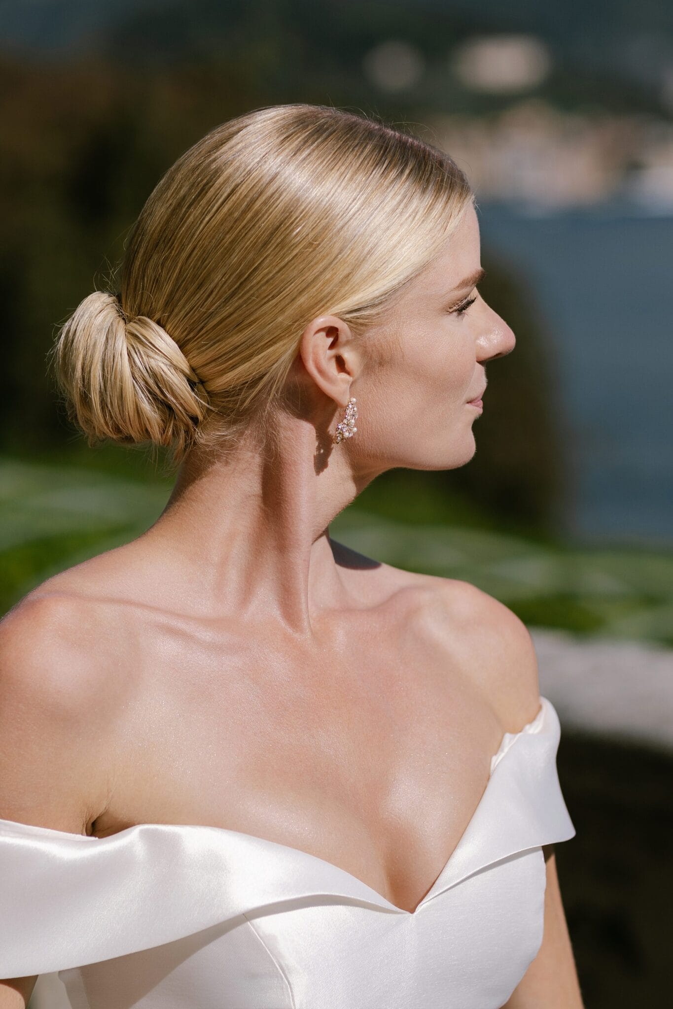 Elegant bridal profile with sleek bun, earrings, and off-shoulder gown at Lake Como.