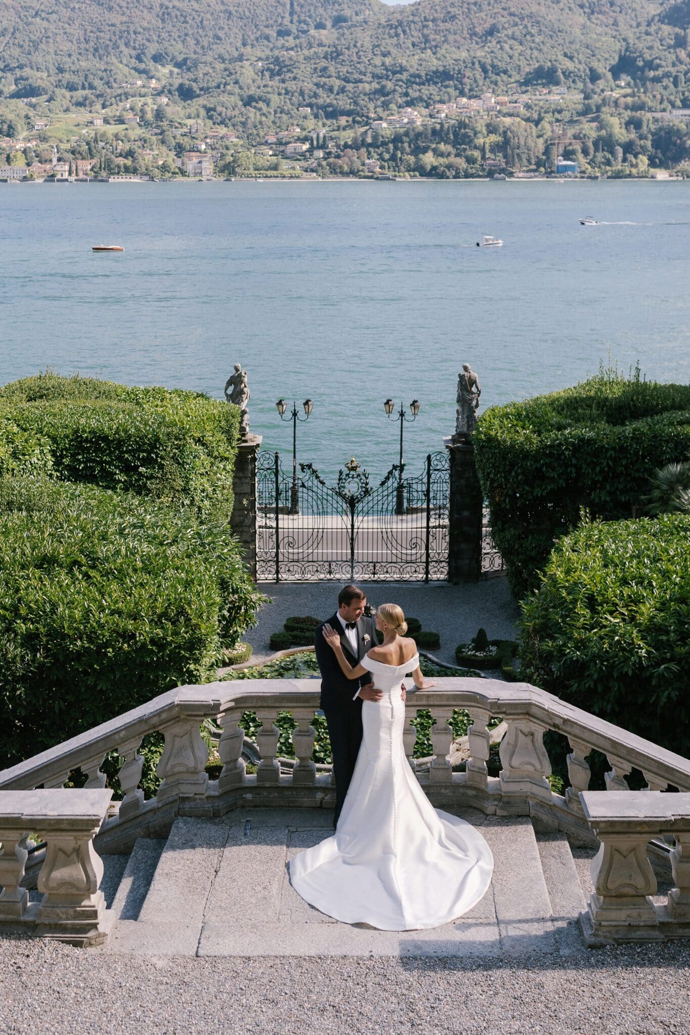 Bride and groom embracing on the stone staircase of Villa Carlotta with Lake Como in the background.