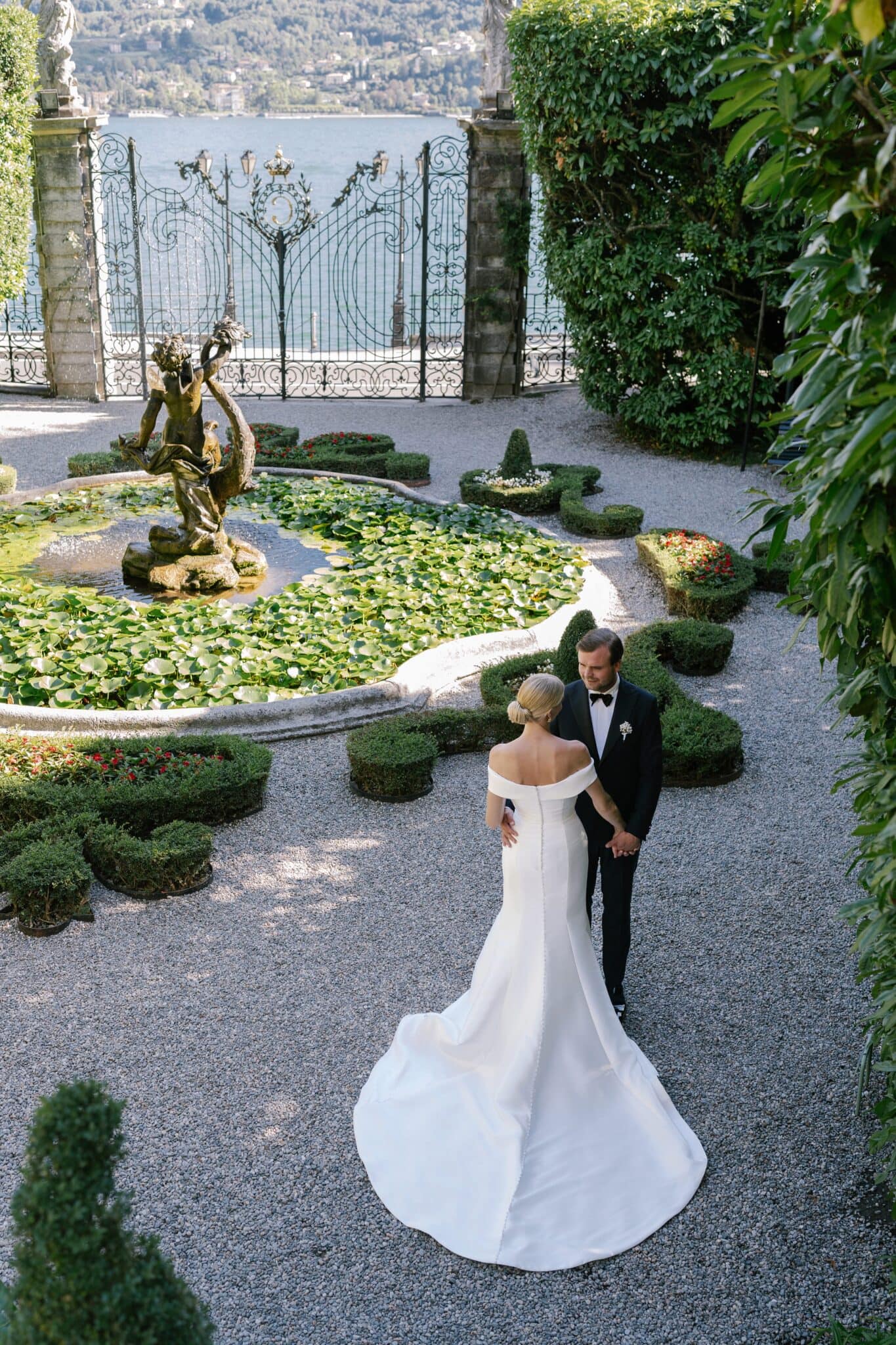Bride and groom standing by the garden fountain with ornate gate at Villa Carlotta.