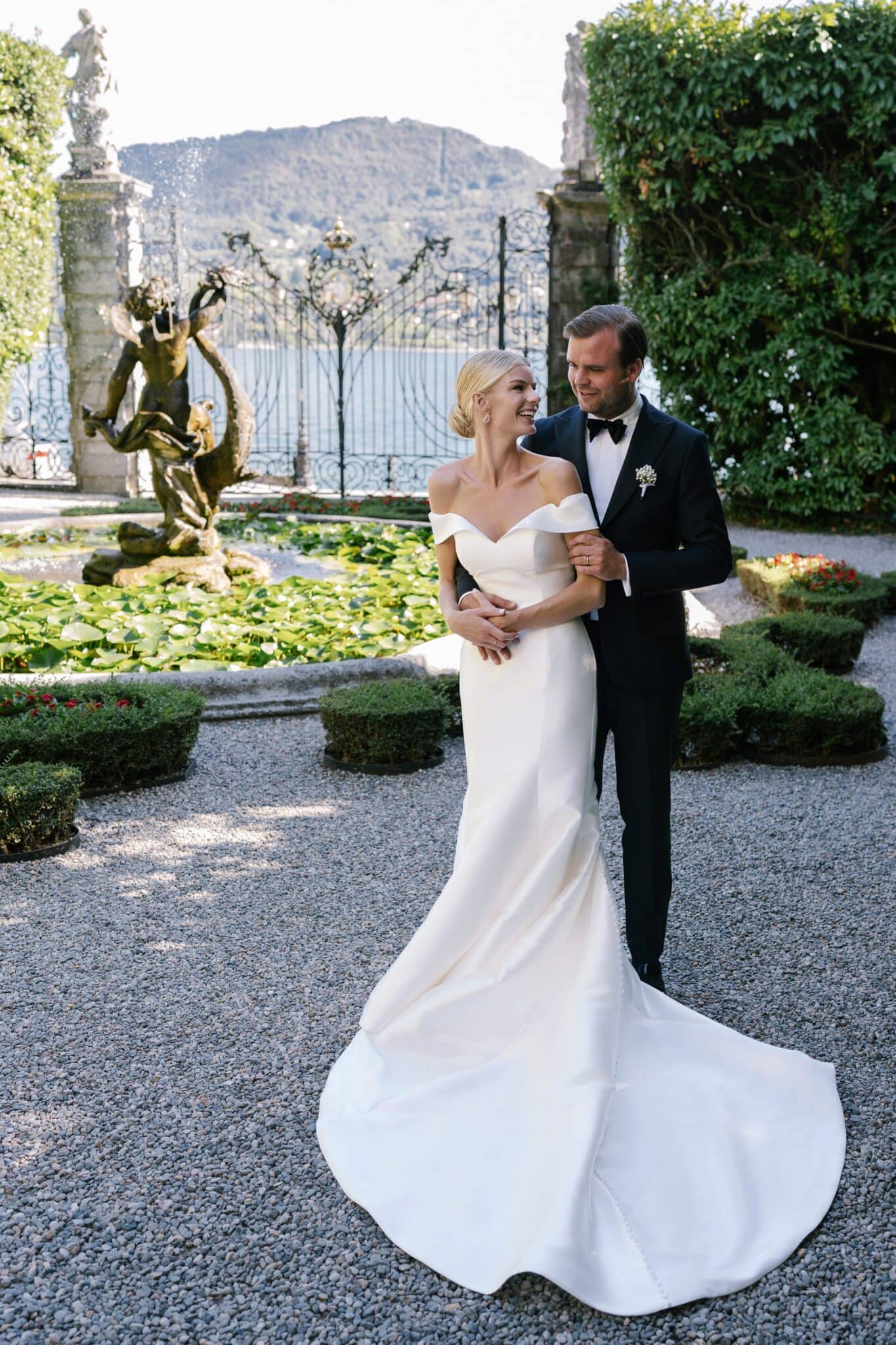 Bride and groom standing together near the fountain in Villa Carlotta gardens with lake view.