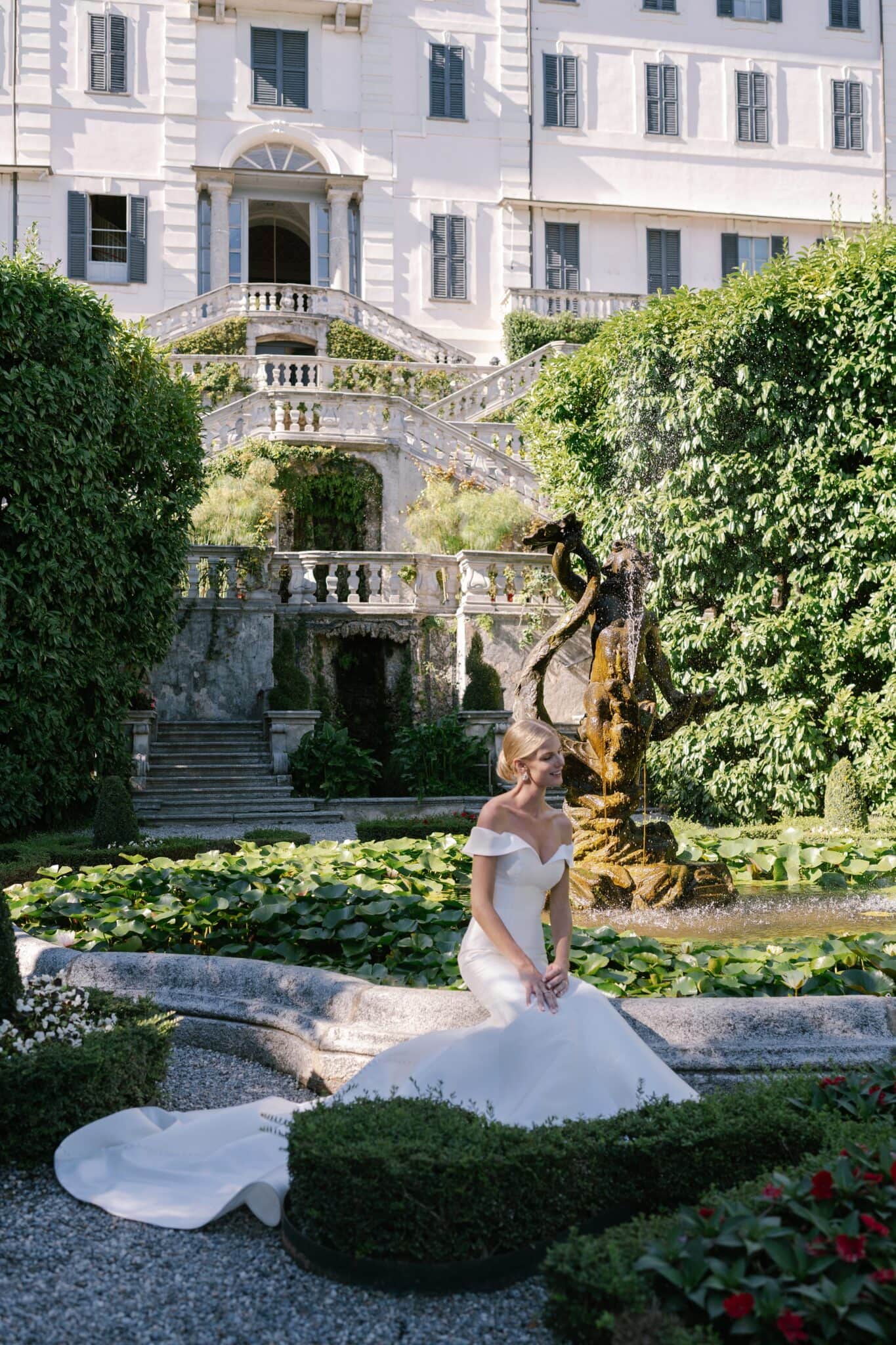Bride sitting gracefully in her gown beside the fountain at Villa Carlotta gardens.