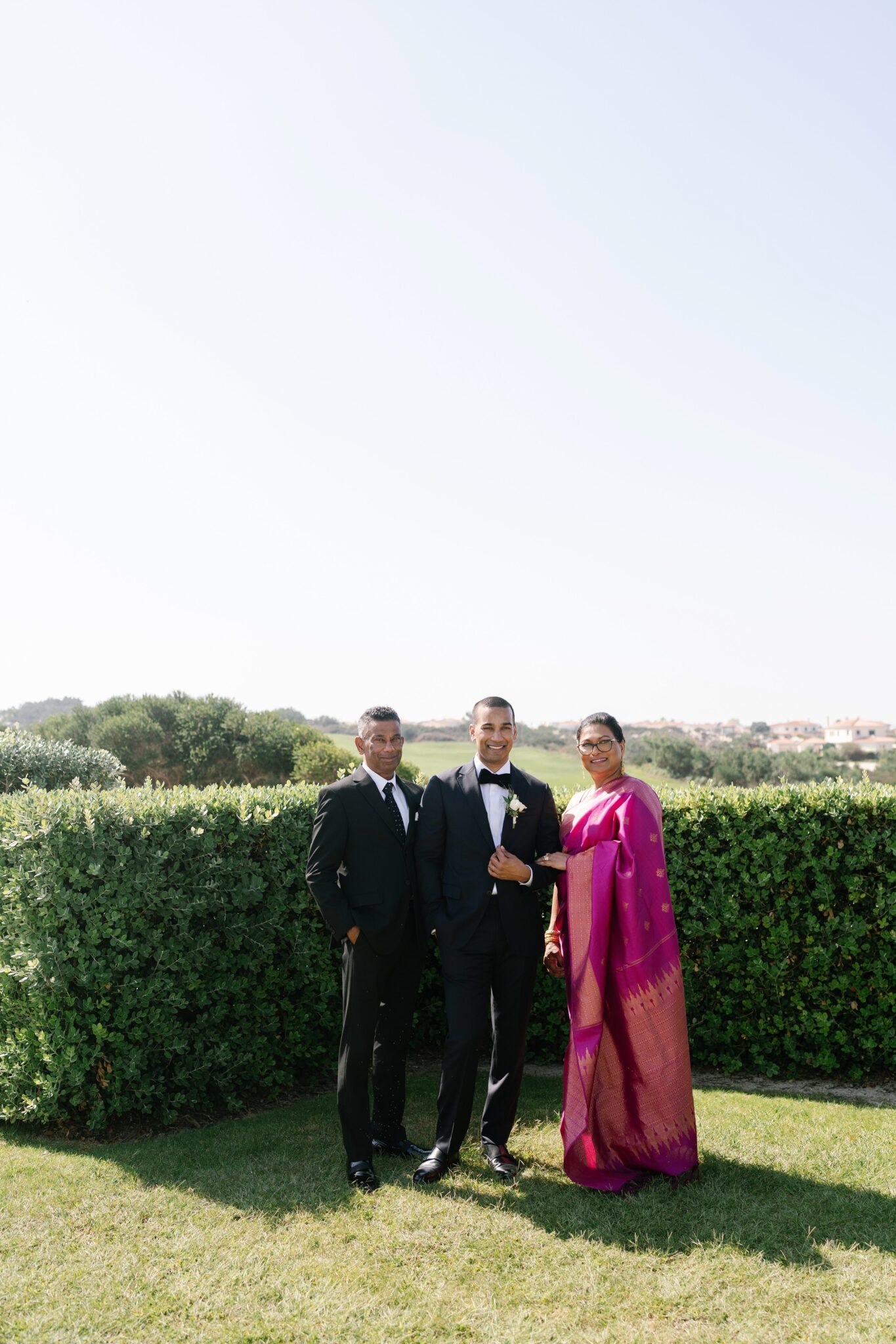 Groom standing with his parents in Portugal garden his mother wearing elegant sari