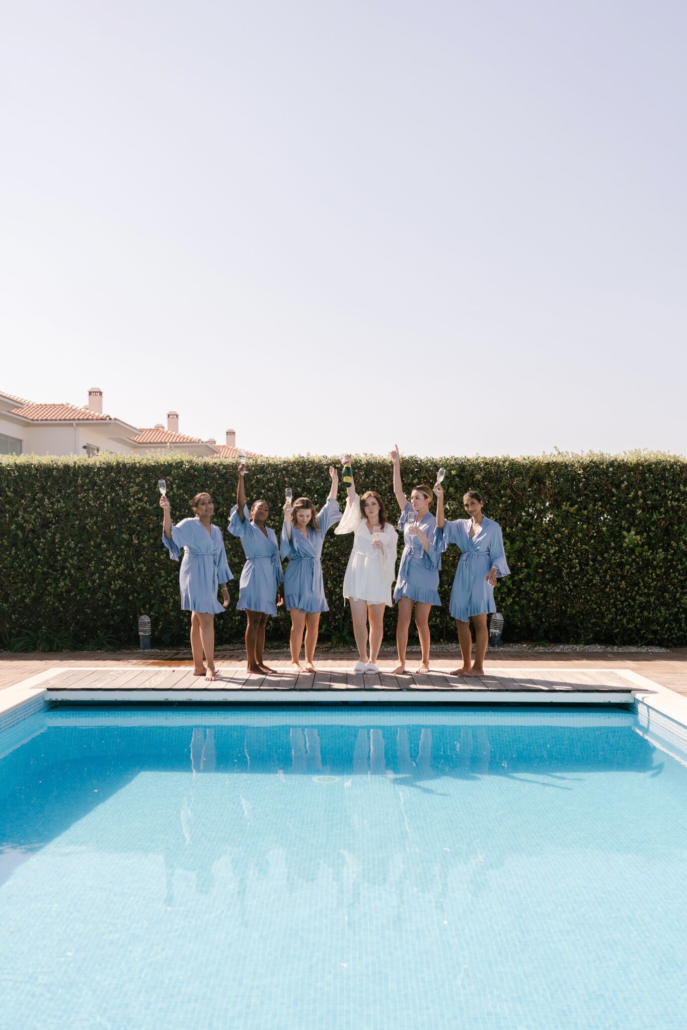 Bride and bridesmaids in blue robes celebrating by the pool on a sunny morning in Portugal