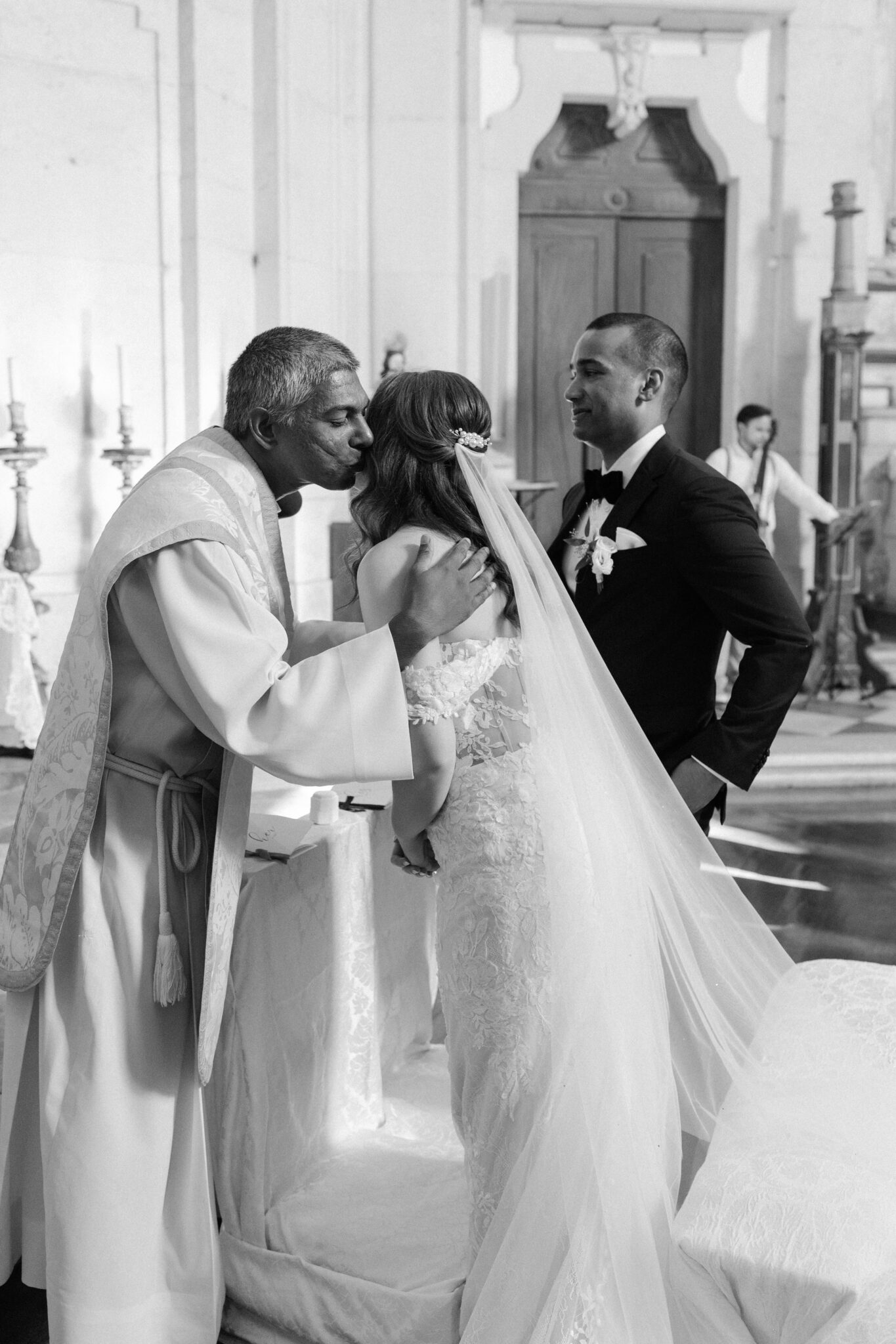 Priest blessing bride with a kiss on the cheek during church ceremony black and white photo in Portugal