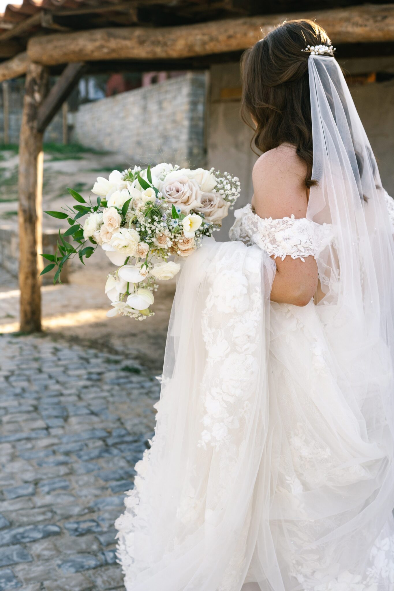 Bride holding her bouquet and lace veil while walking through cobblestone streets of Obidos in Portugal