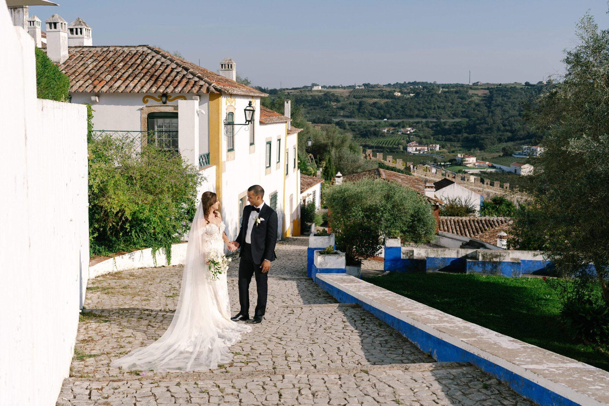 Bride and groom walking hand in hand along a cobblestone street in a historic town Obidos in Portugal