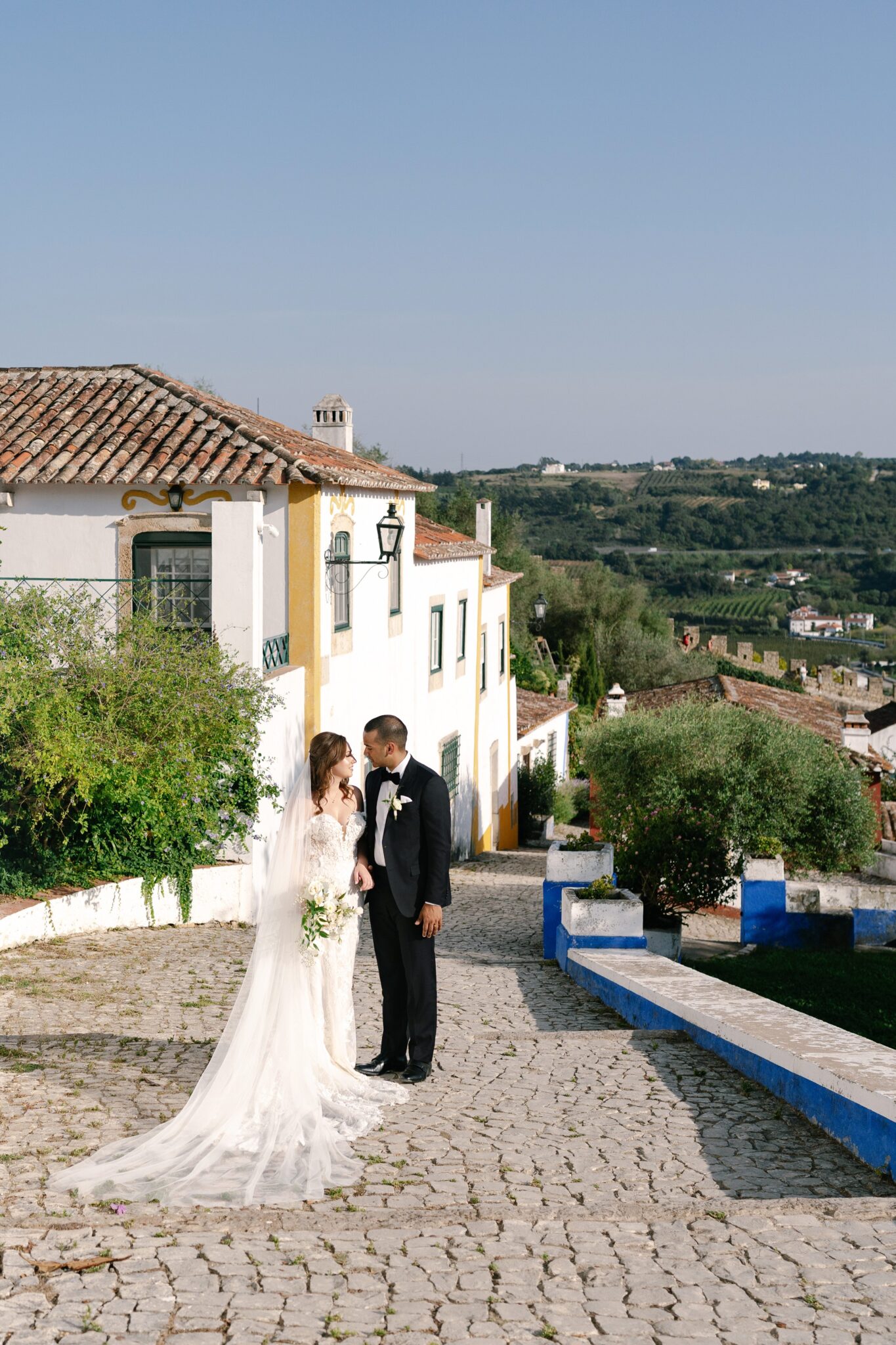 Bride and groom walking along cobblestone street with historic houses in Óbidos Portugal
