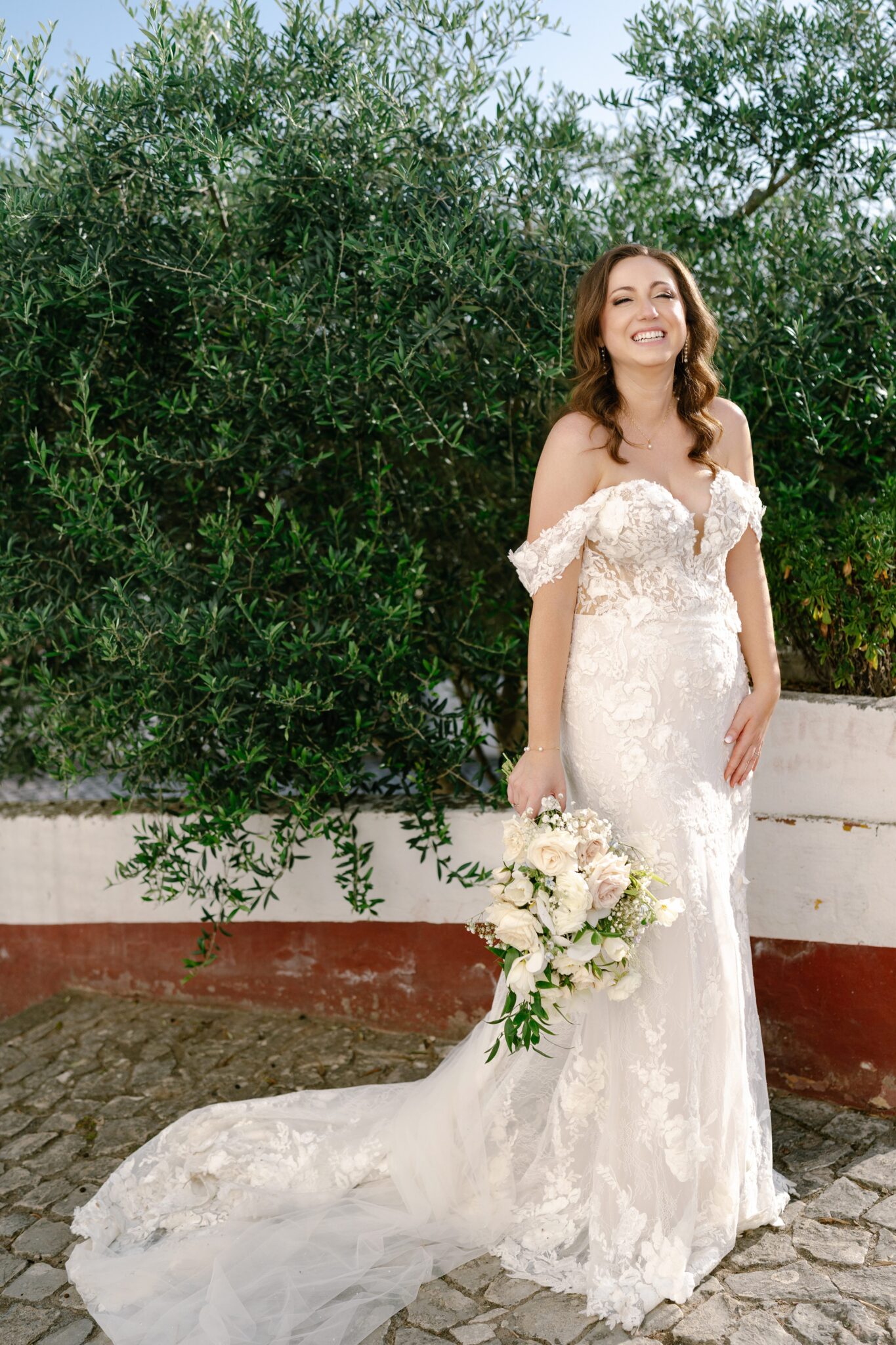 Bride standing in cobblestone street with flowing lace gown and bouquet in Óbidos, Portugal