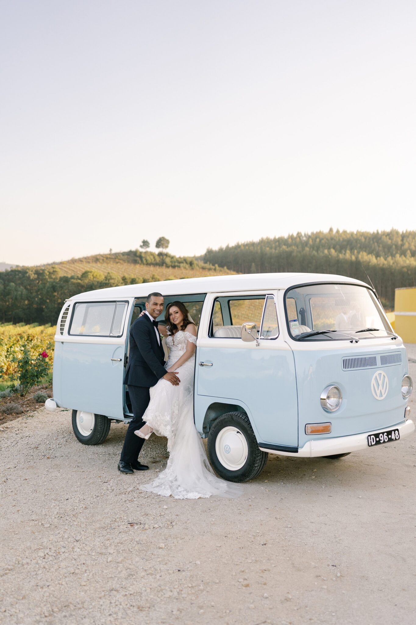 Bride and groom embracing by vintage blue VW van at vineyard wedding in Portugal