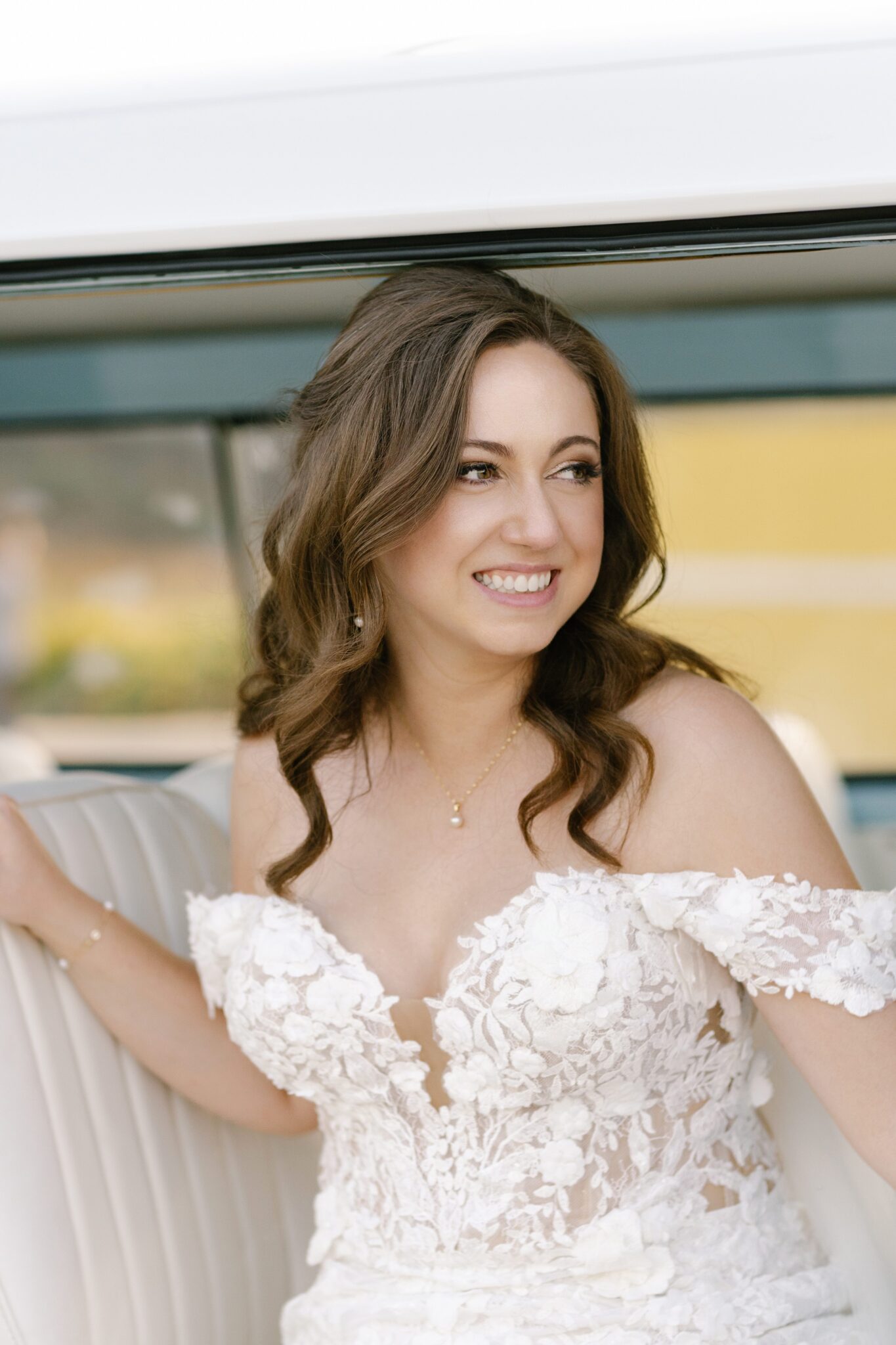 Bride in lace off-the-shoulder wedding dress smiling while stepping out of vintage blue Volkswagen van