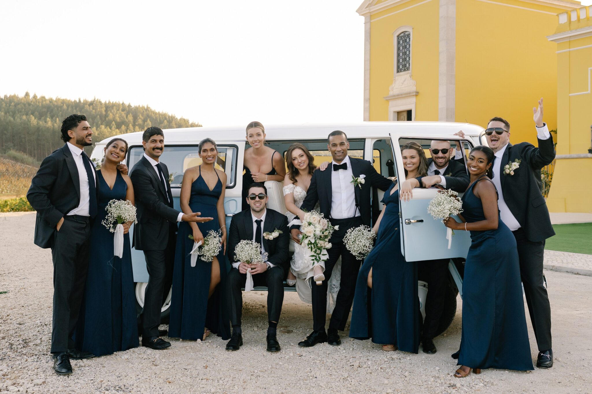Bridesmaids and groomsmen in navy attire celebrating with couple by vintage van in Portugal