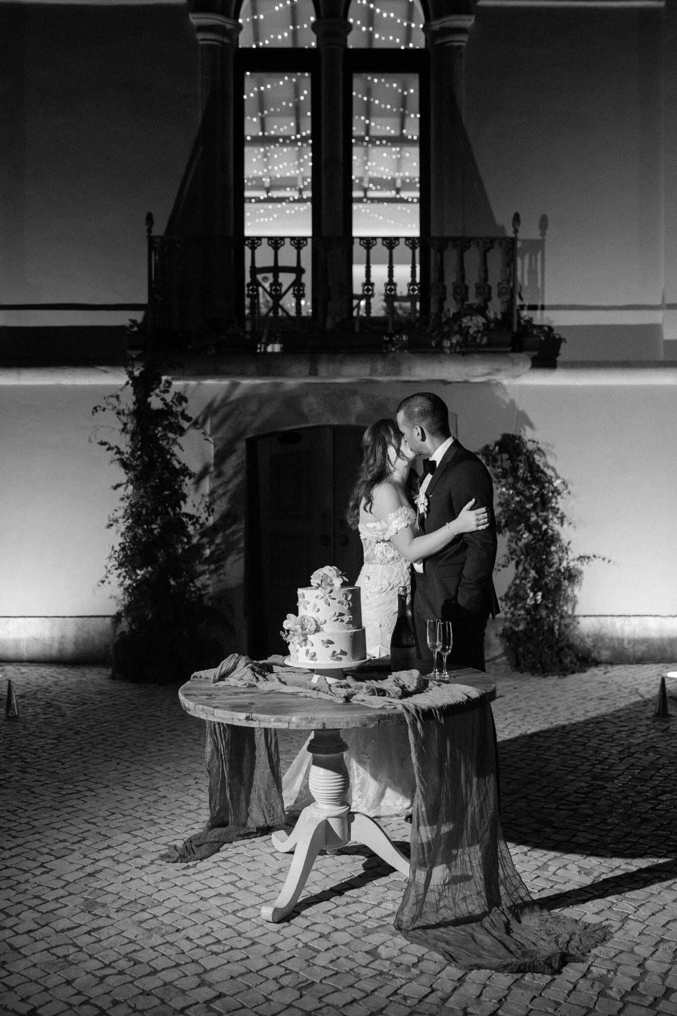 Newlyweds kissing by the wedding cake in a romantic black and white shot