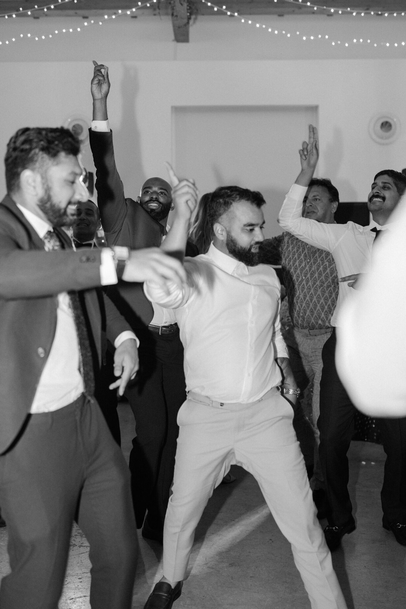Groomsmen and guests dancing energetically at Portugal wedding party black and white photo