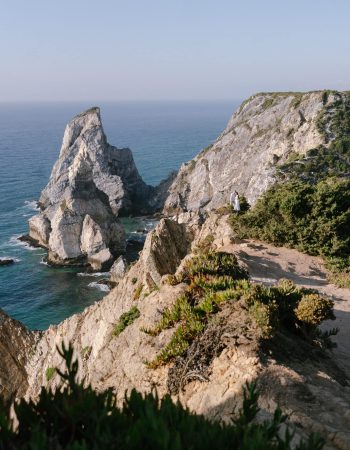 A couple standing on the dramatic cliffs of Praia da Ursa in Sintra, overlooking the Atlantic Ocean and iconic rock formations. Title: Praia da Ursa Elopement on the Cliffs of Sintra | Yana Yart